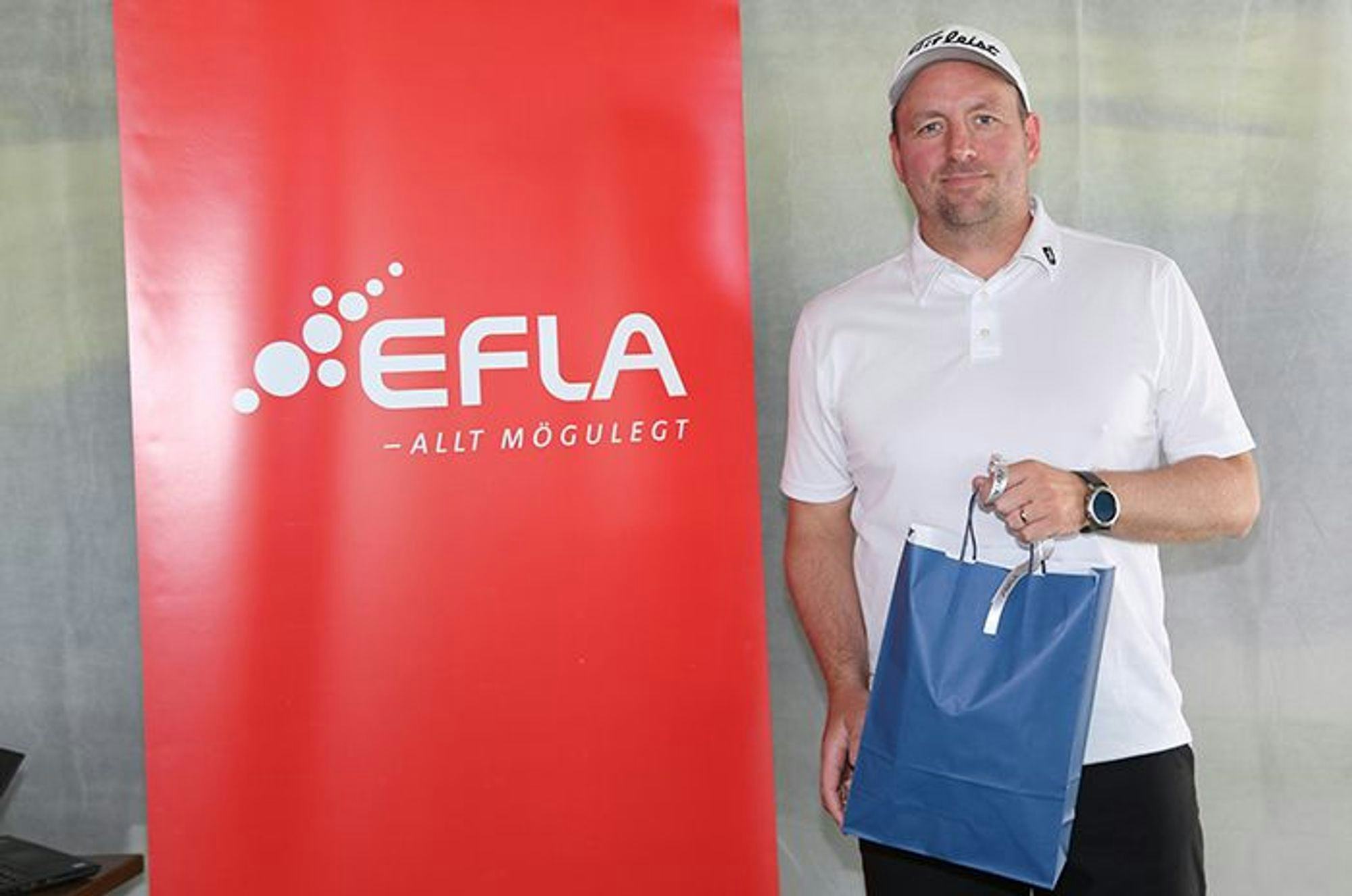 A man holding a blue bag, standing next to EFLA red promotional banner