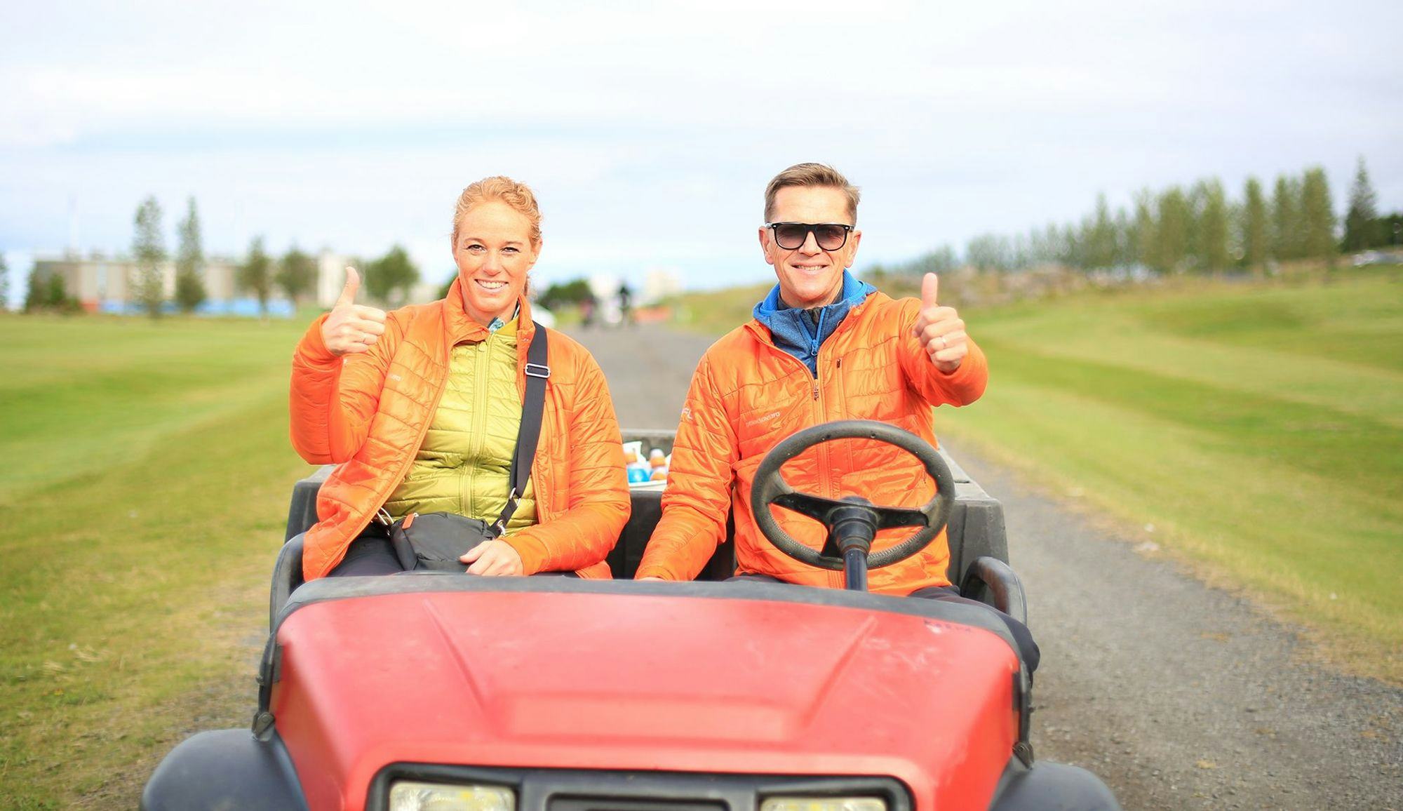 Two individuals sitting in a golf cart, giving thumbs up