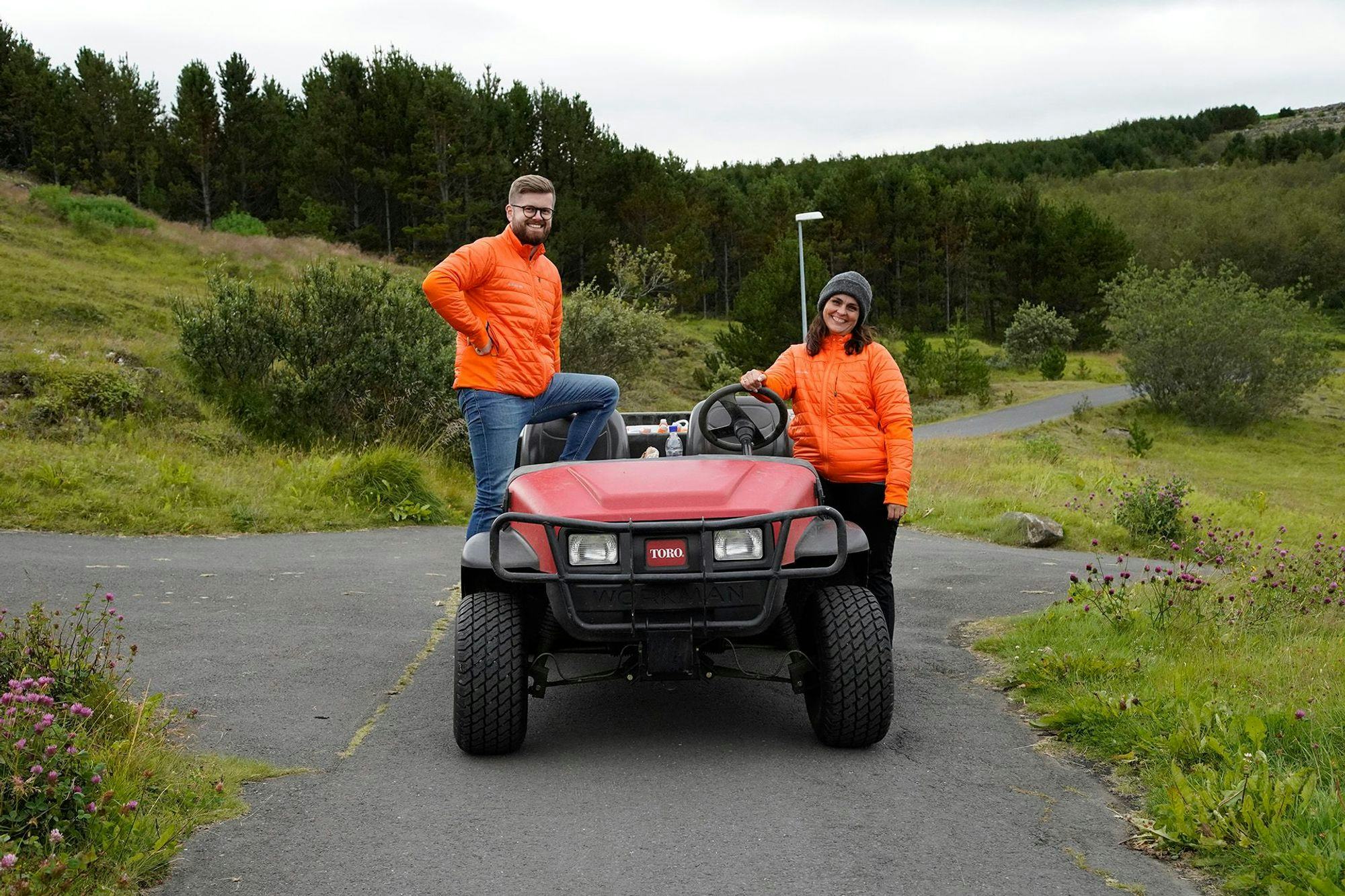 Two individuals in a bright orange jacket standing next to a red golf cart