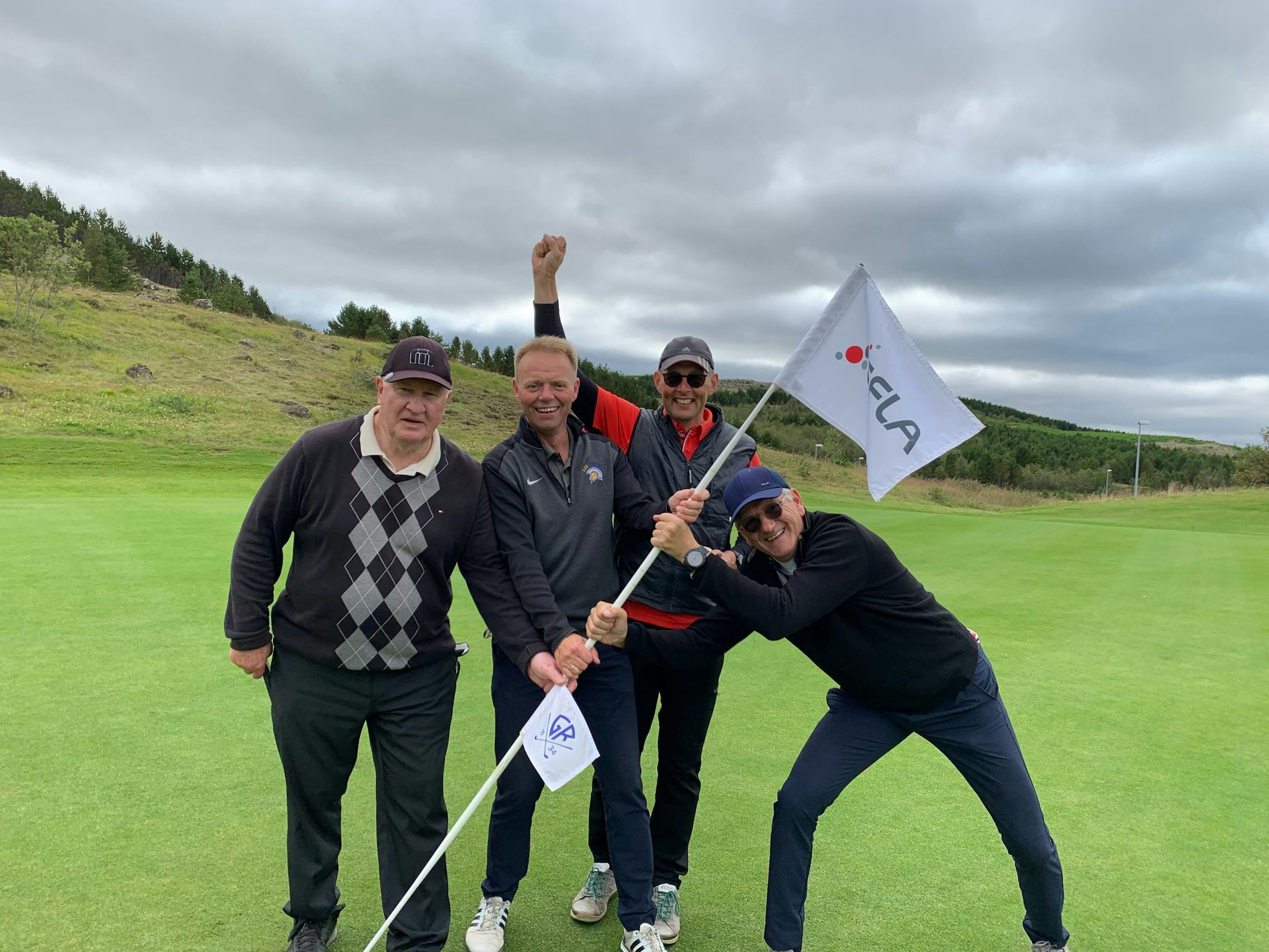 Four men posing joyfully on a golf course with one of them holding a flagstick