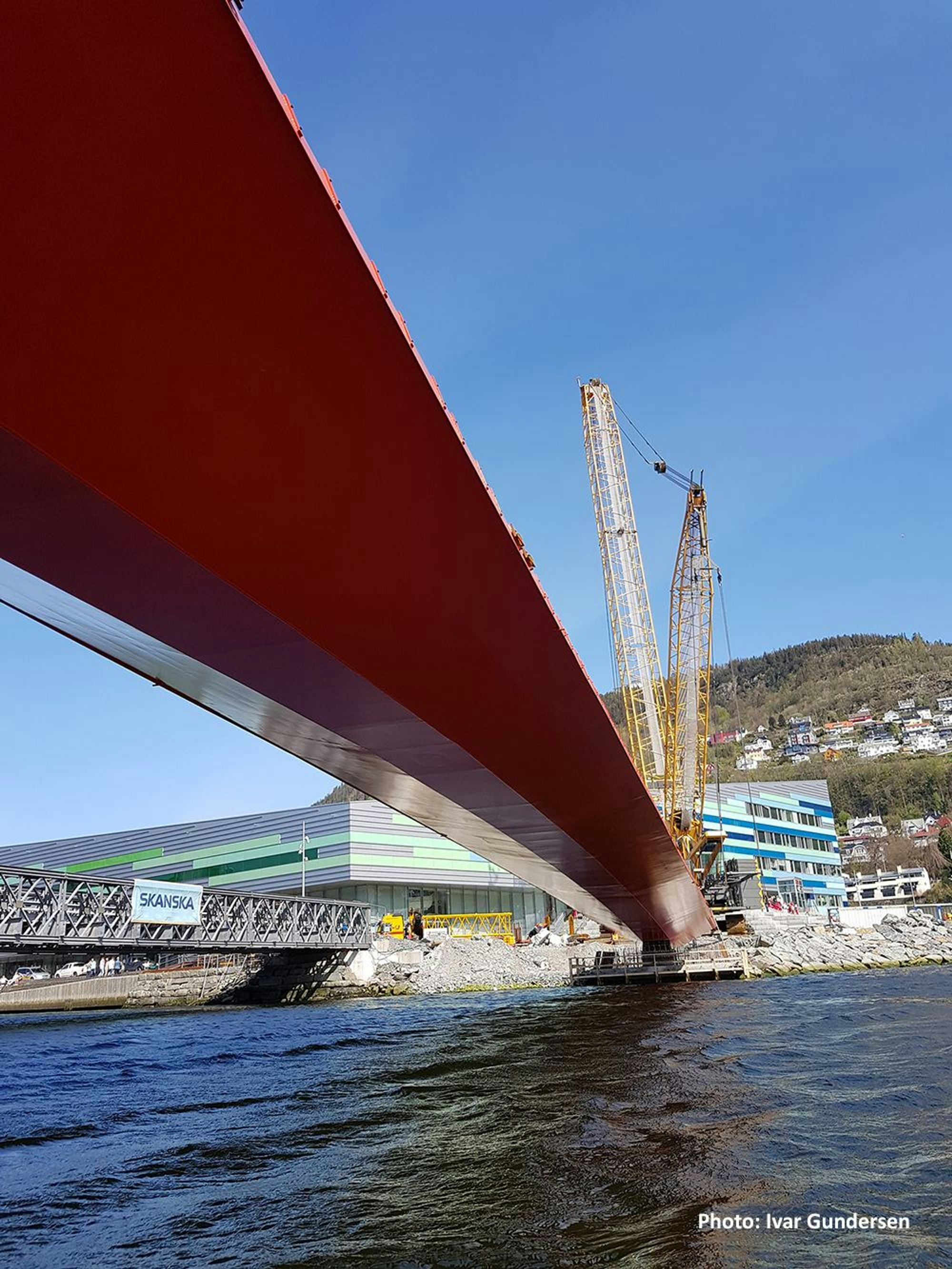 A large red bridge under construction with the aid of cranes