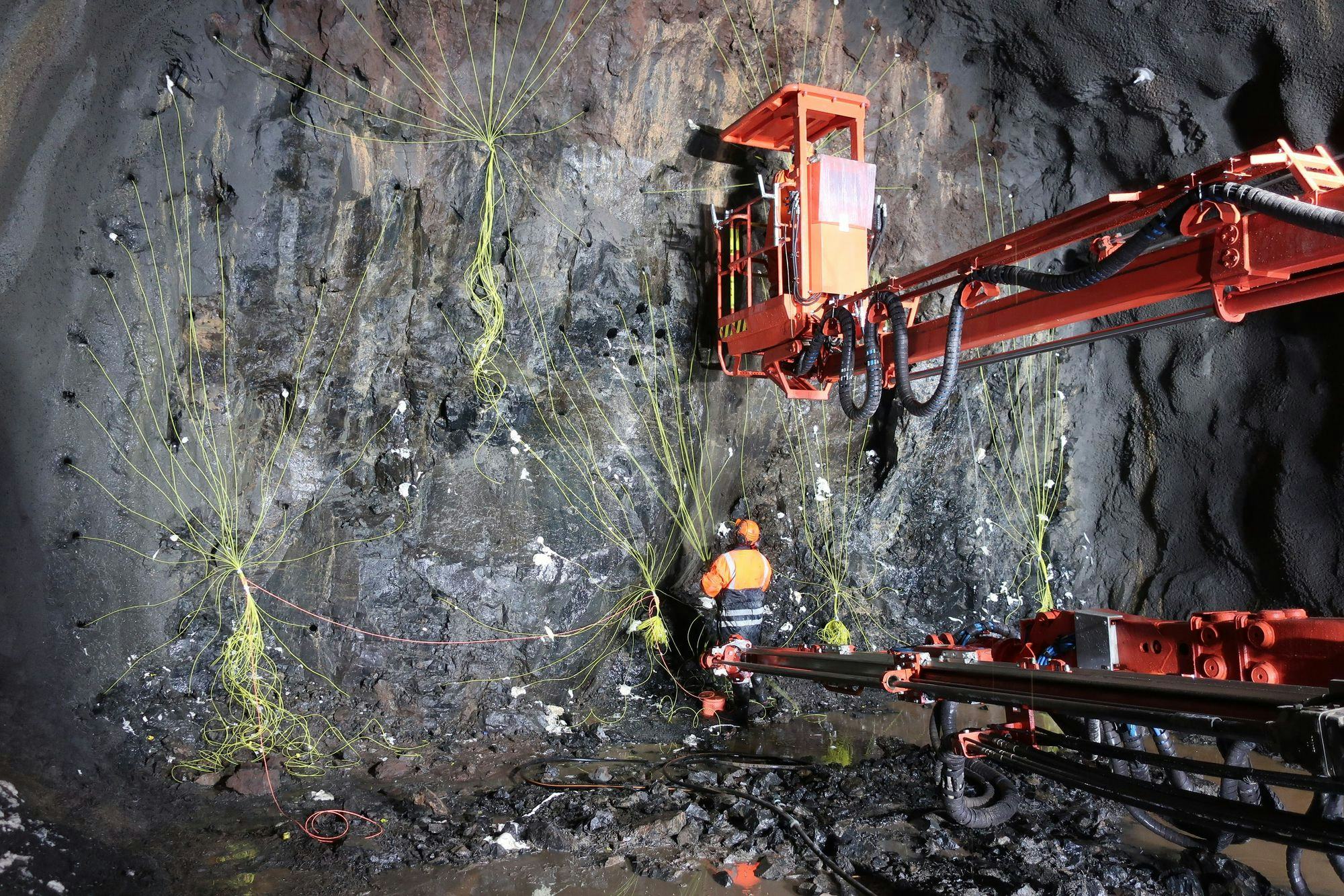 Construction worker next to a red drilling rig, reinforcing a rocky wall with green material