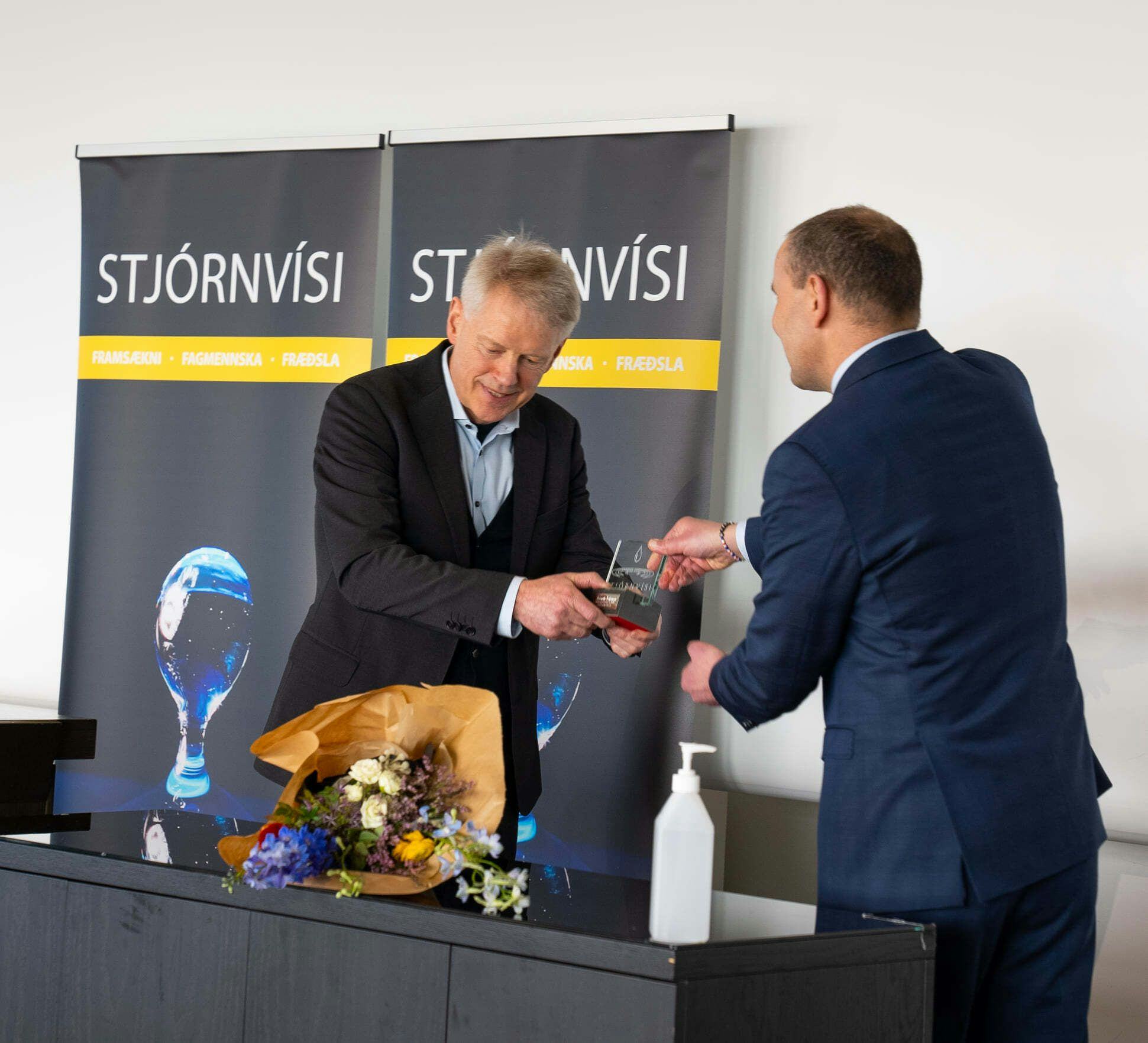 The photo captures an event where one man is handing a small trophy to another
