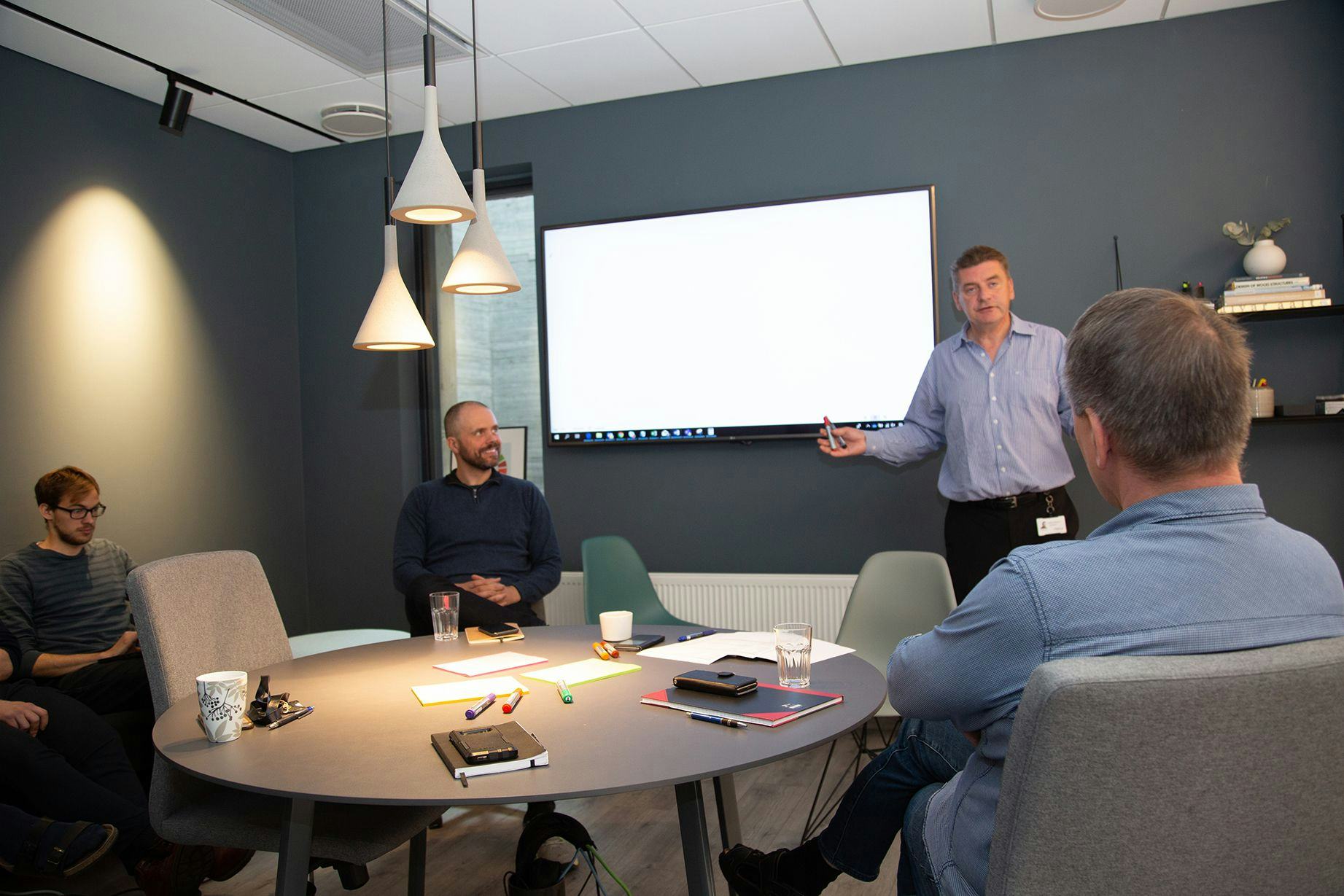 A man presenting to a small group of people in a meeting room with big screen and modern decor