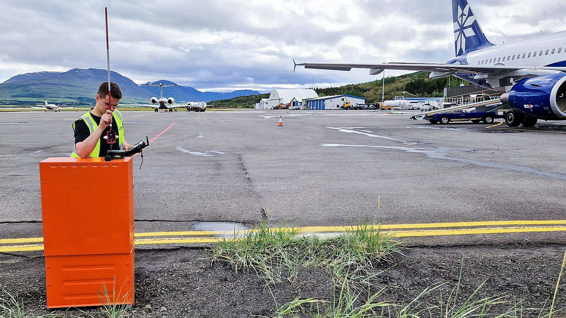 A ground crew member communicating via radio with aircraft and airport facilities in the background