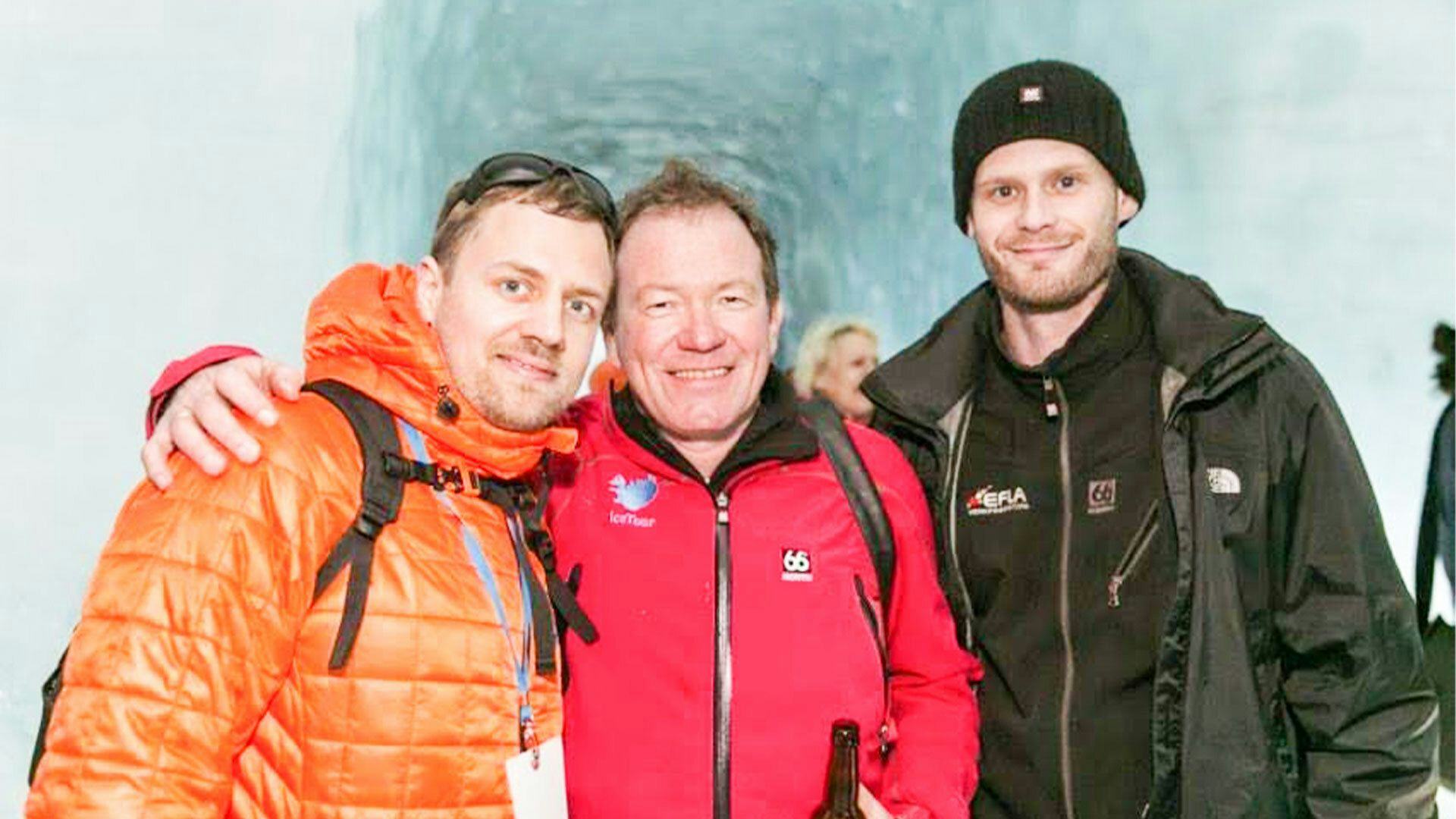 Three men in warm clothing posing with a blurred icy background 