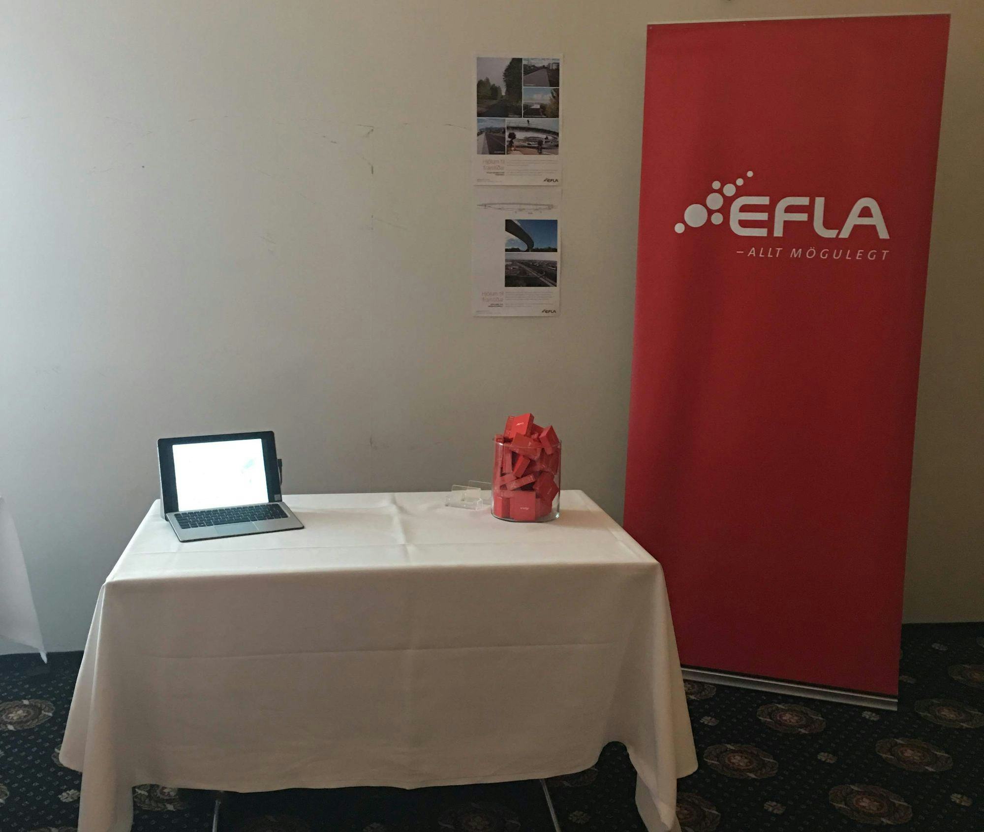 Image shows registration or information table with a laptop and red packages in a glass container