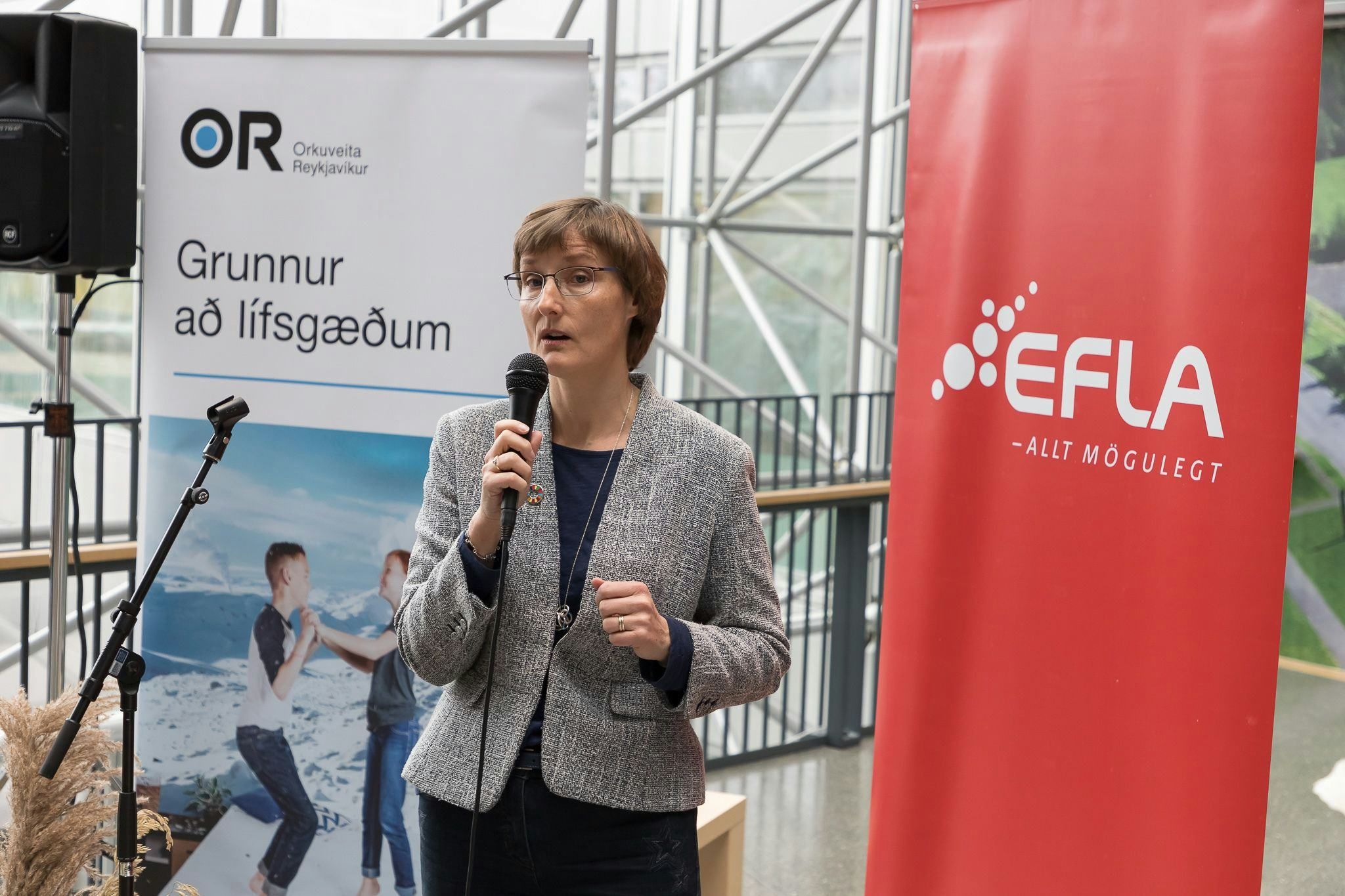A woman speaking into a microphone in front of promotional banners