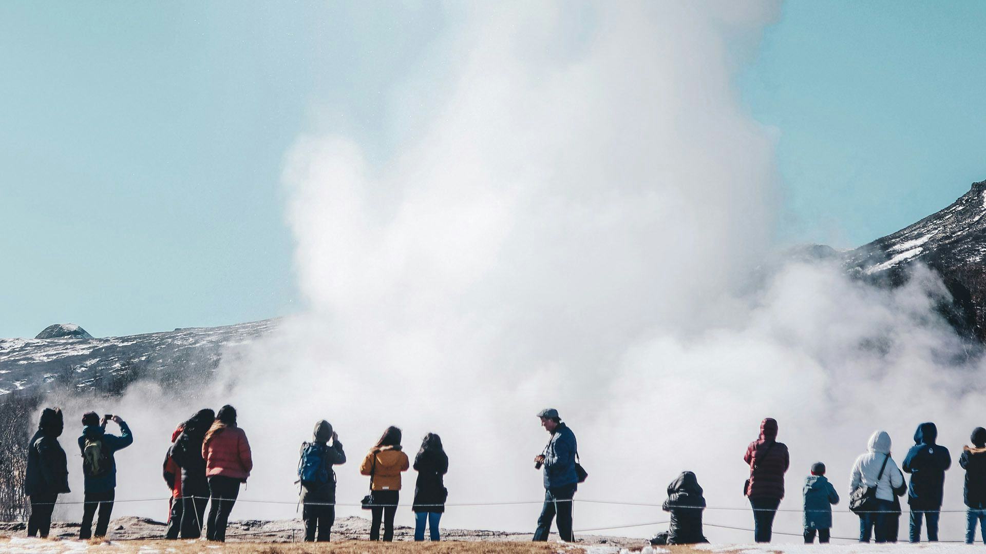 A large group of people observing geyser eruption in a snowy landscape 