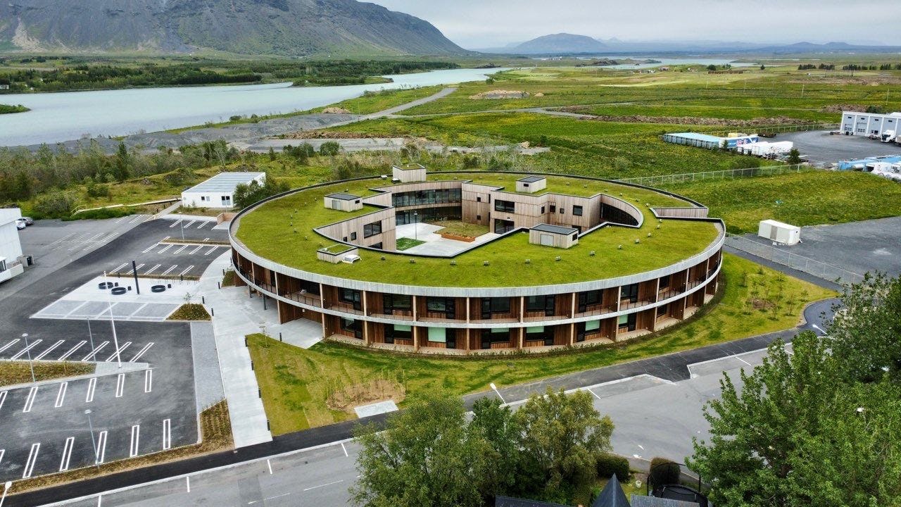 A circular building with green roof, integrated into a natural landscape with a river and mountain in the background