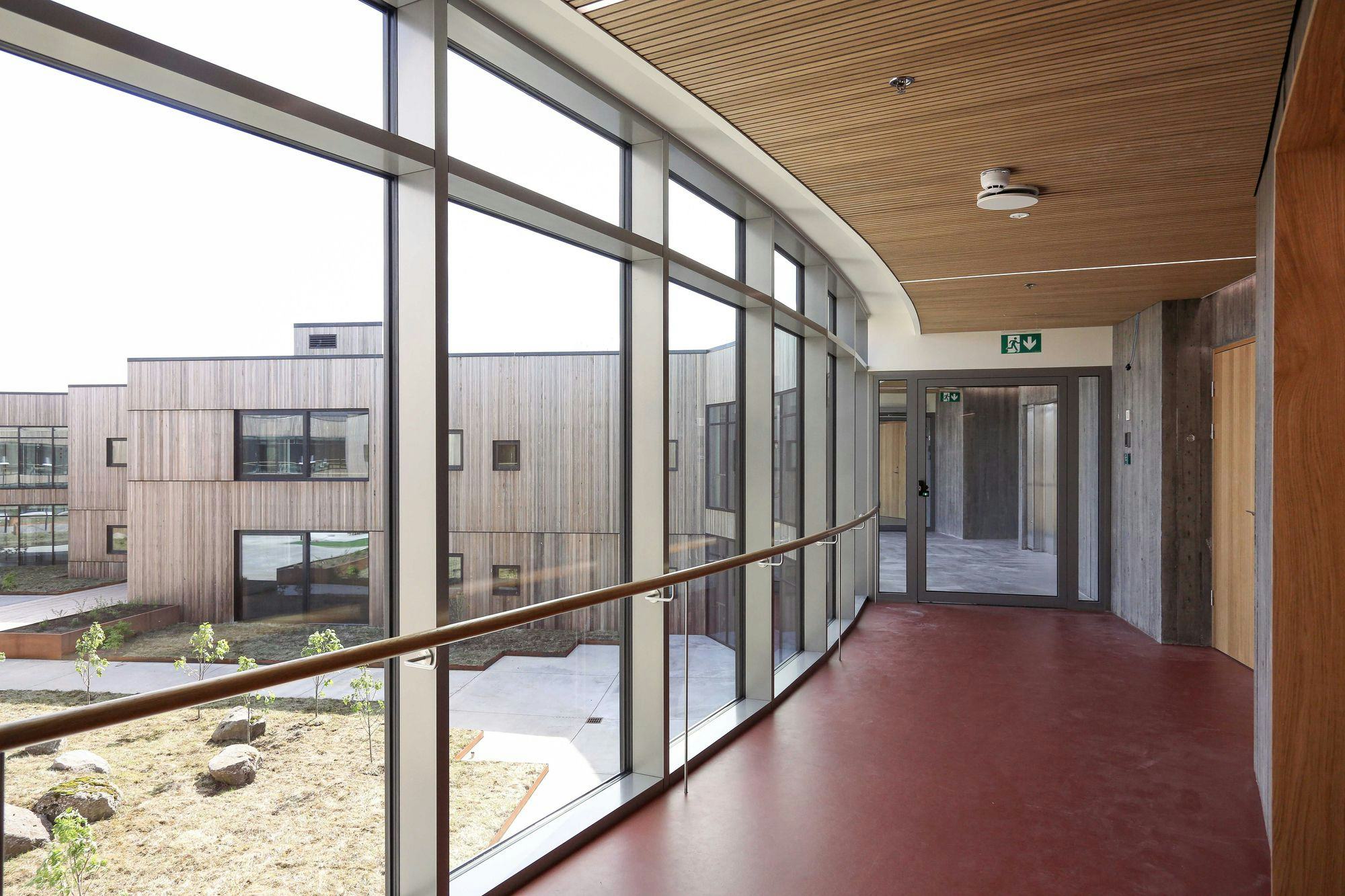 An interior corridor with a curved glass wall on one side, offering view of a courtyard