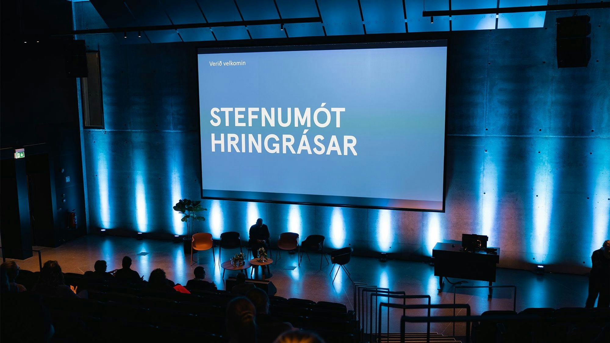 A dark auditorium with a large presentation screen displaying the title "STEFNUMOT HRINGRASAR"