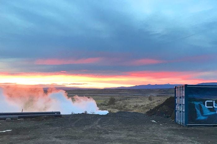 A geothermal power plant featuring steam rising from the ground against vivid sunset