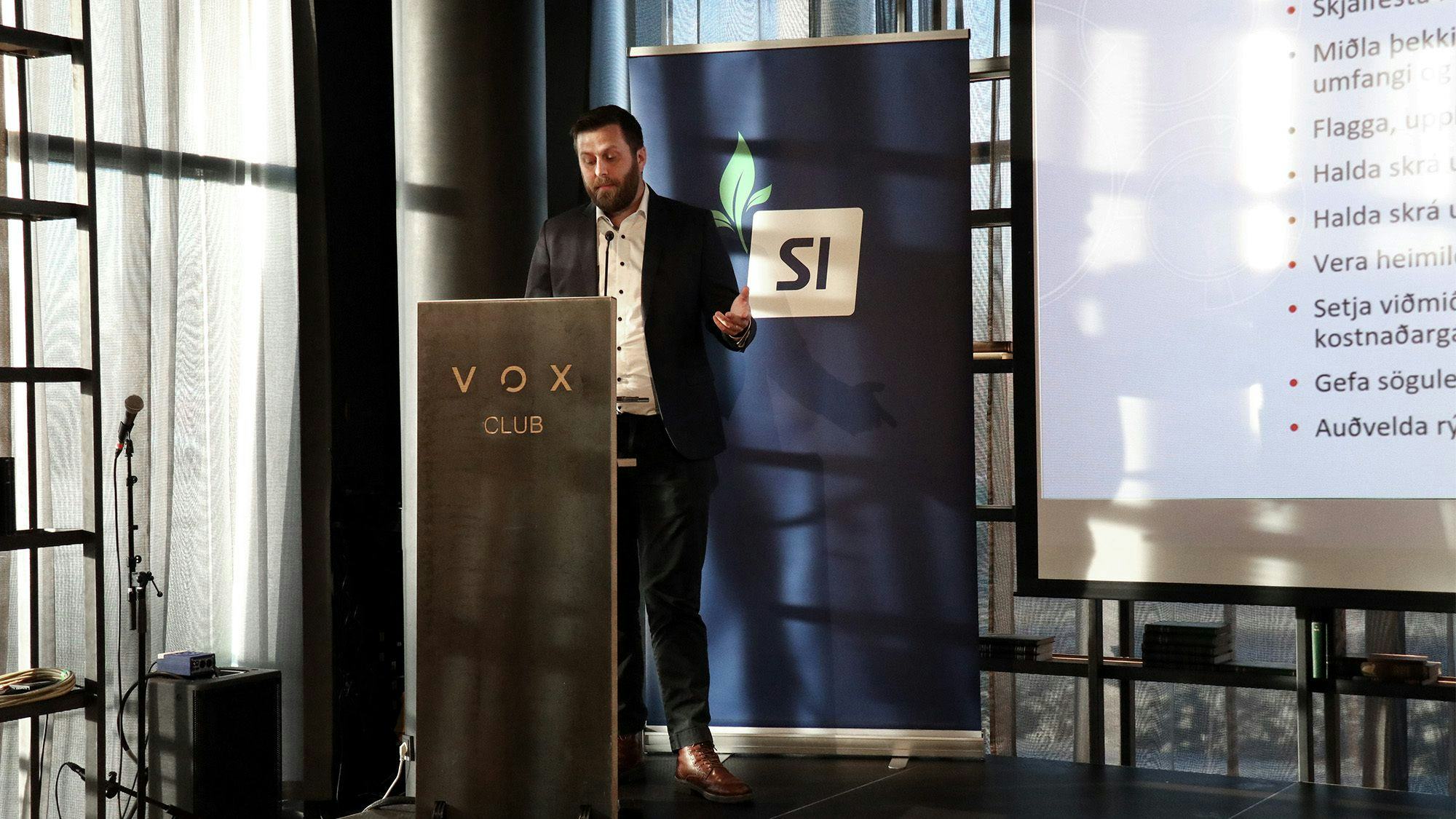 A man standing behind a lectern with "VOX CLUB" on the front, 
