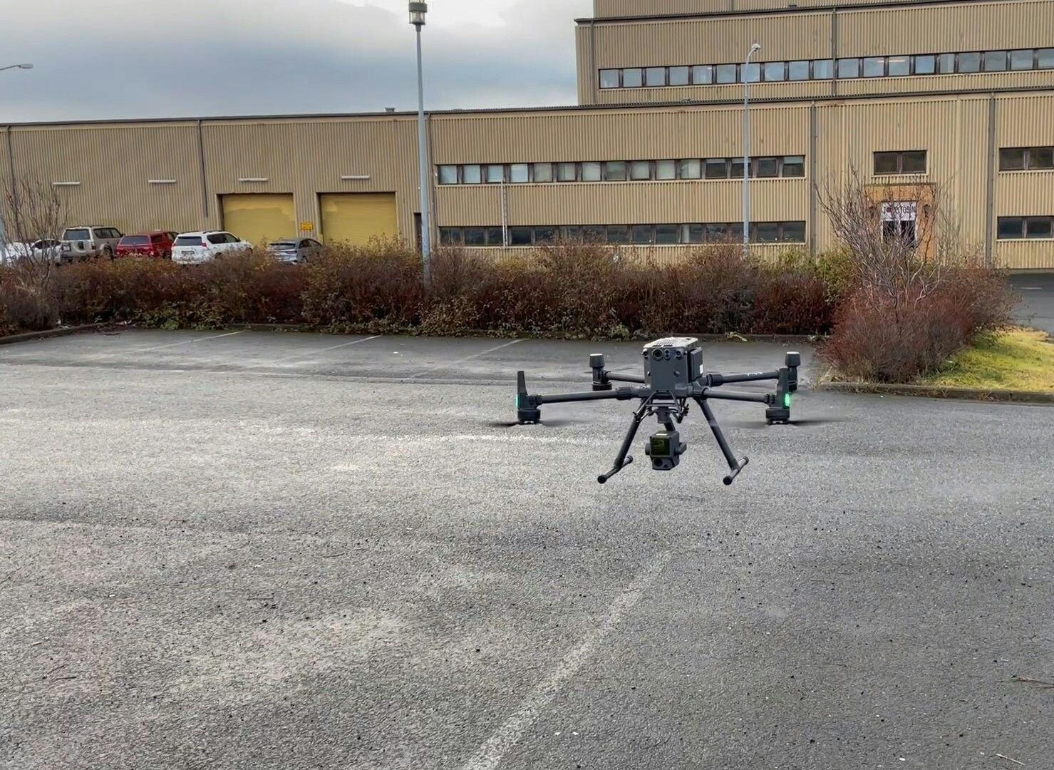 A black drone mid flight in front of an industrial building