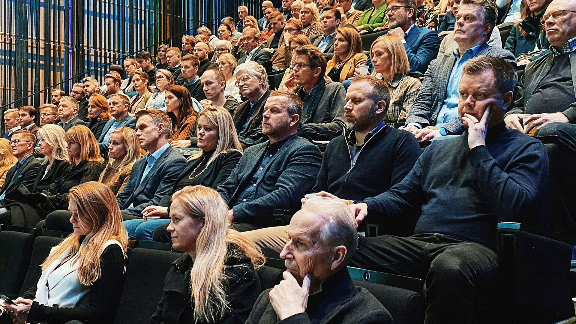 A large audience seated in rows at a conference, where some people are focused