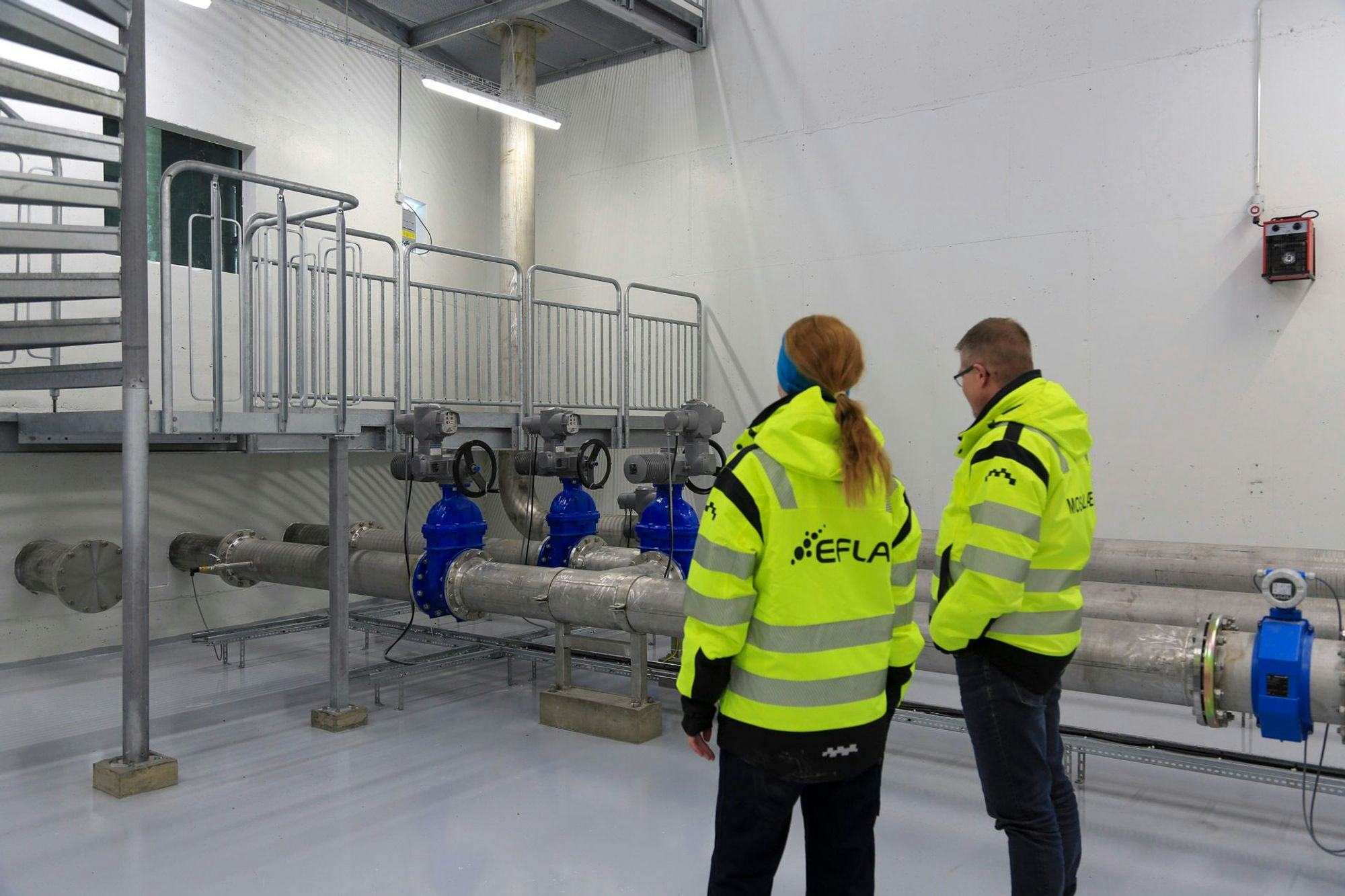 Two individuals in high visibility jacket inspecting industrial pipping and valves