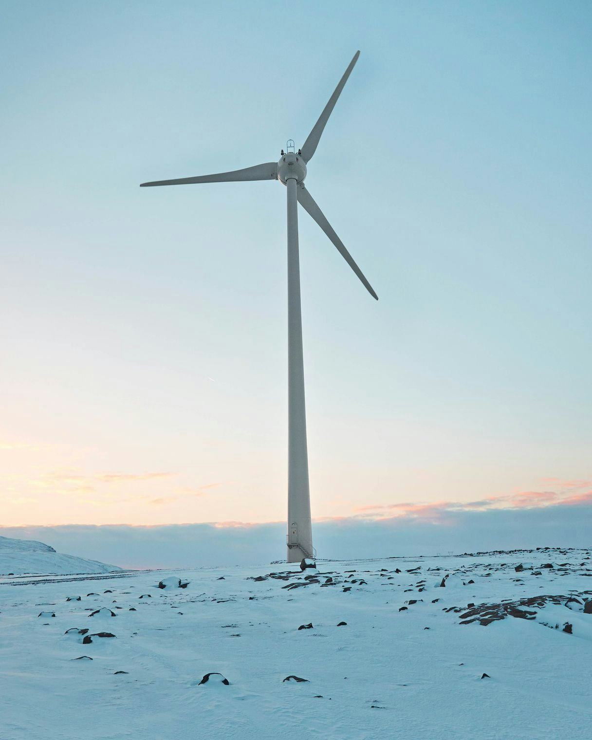 A single wind turbine against a snowy landscape with low sun on the horizon