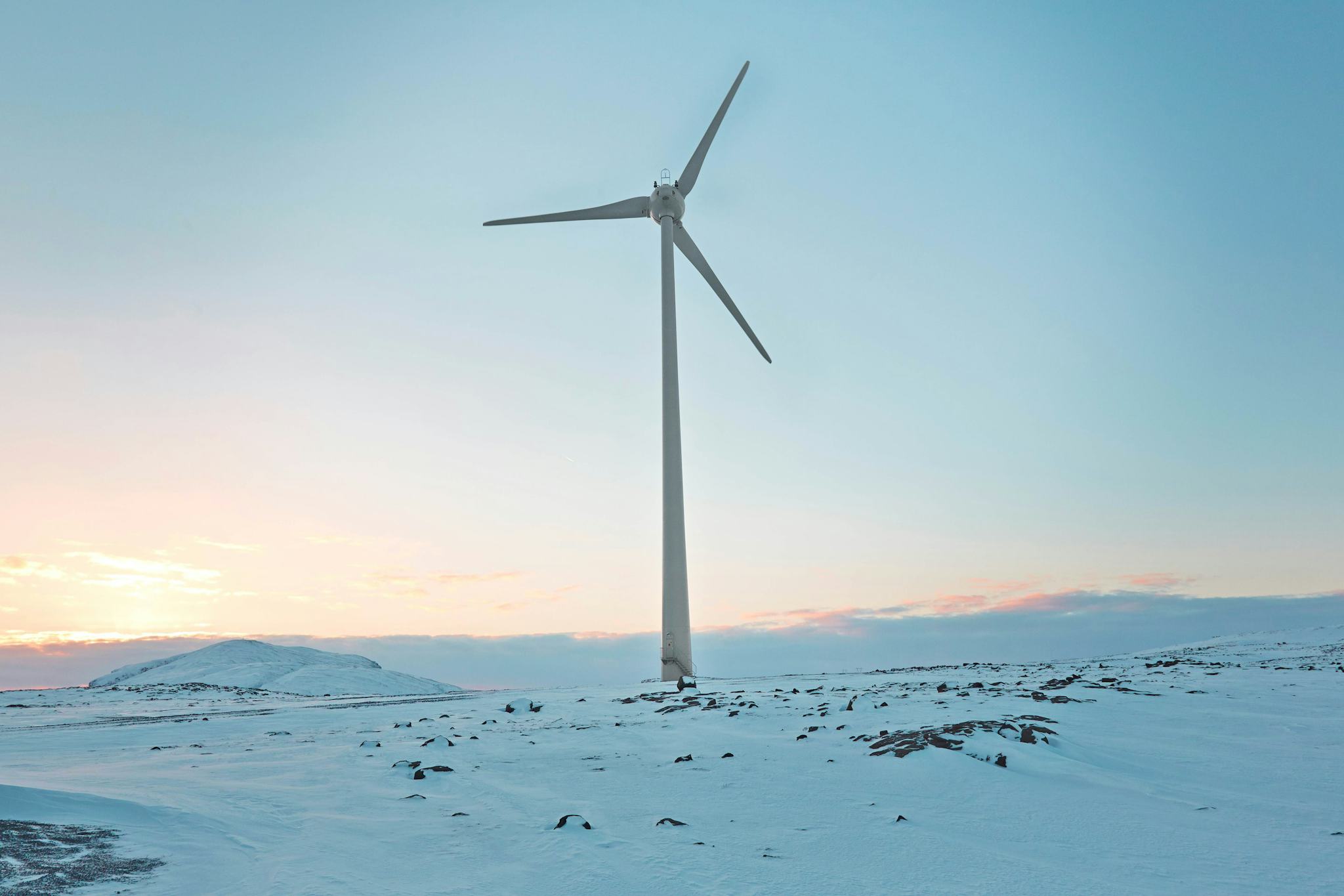 A single wind turbine against a snowy landscape with low sun on the horizon