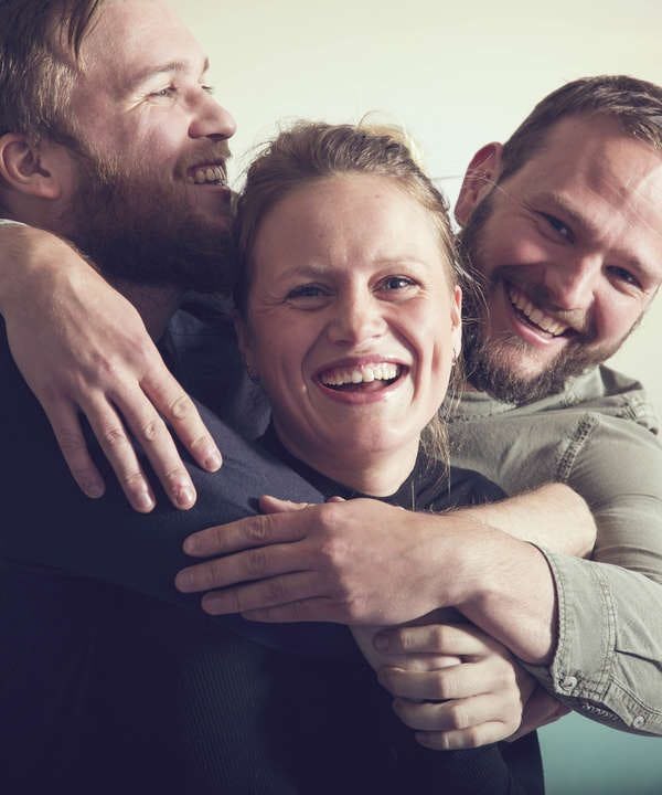 Two men and a woman hugging with smile on their faces