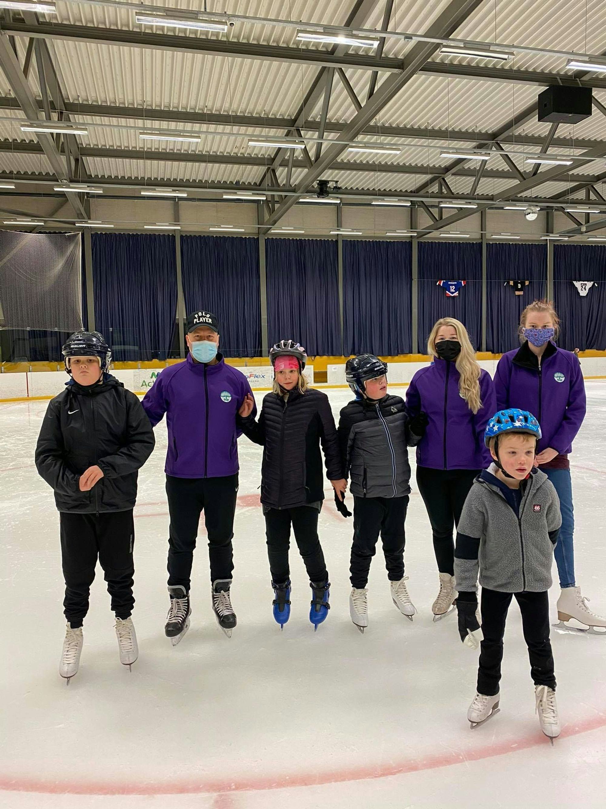 A group of people with protective gear and masks, standing on an indoor ice rink