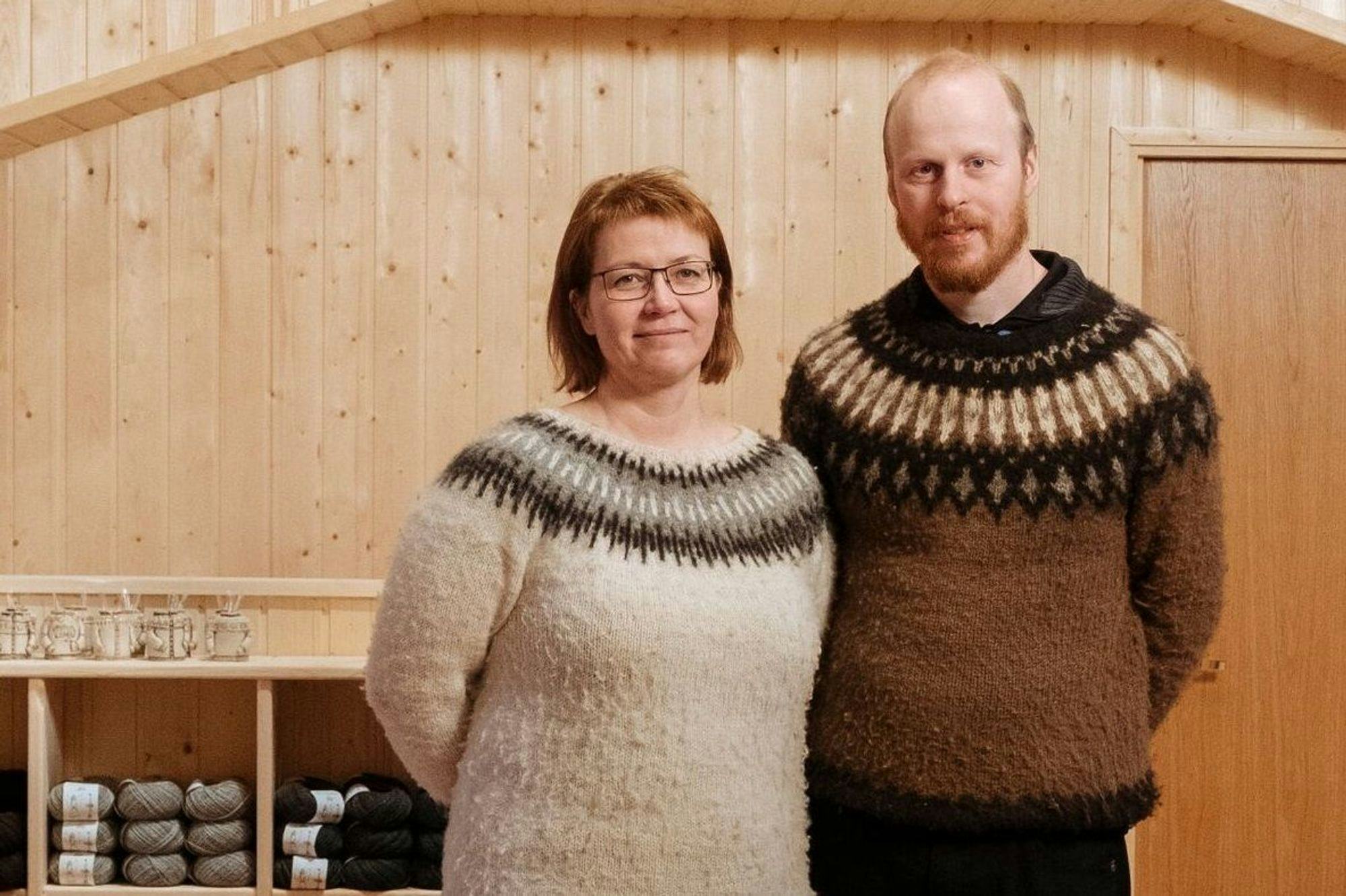A man and a woman wearing traditional patterned Icelandic sweaters standing in a room with a wooden interior