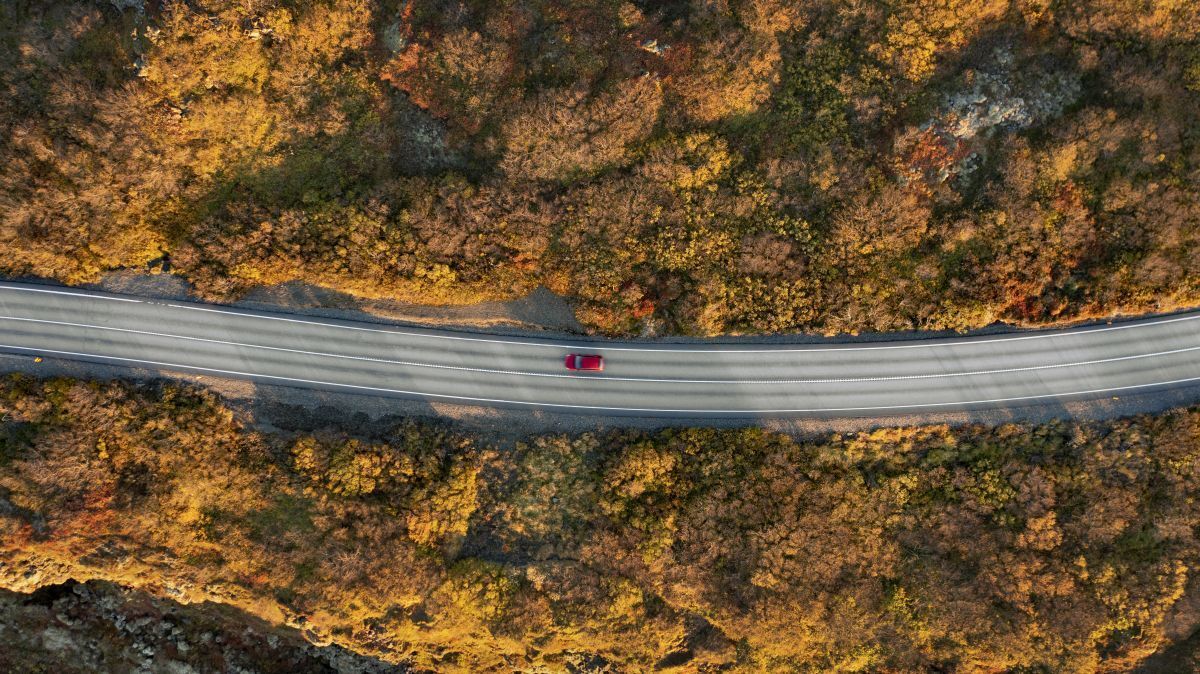 A red car cruising on a road that cuts through a landscape with brown vegetation