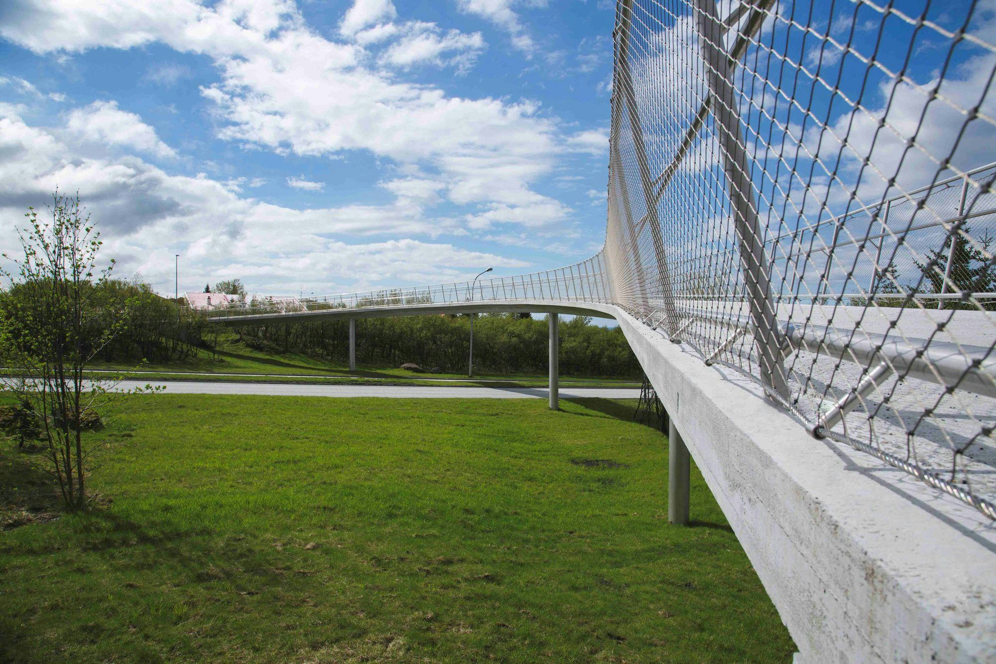 A pedestrian bridge with a unique curved design on a sunny day with partly cloudy sky