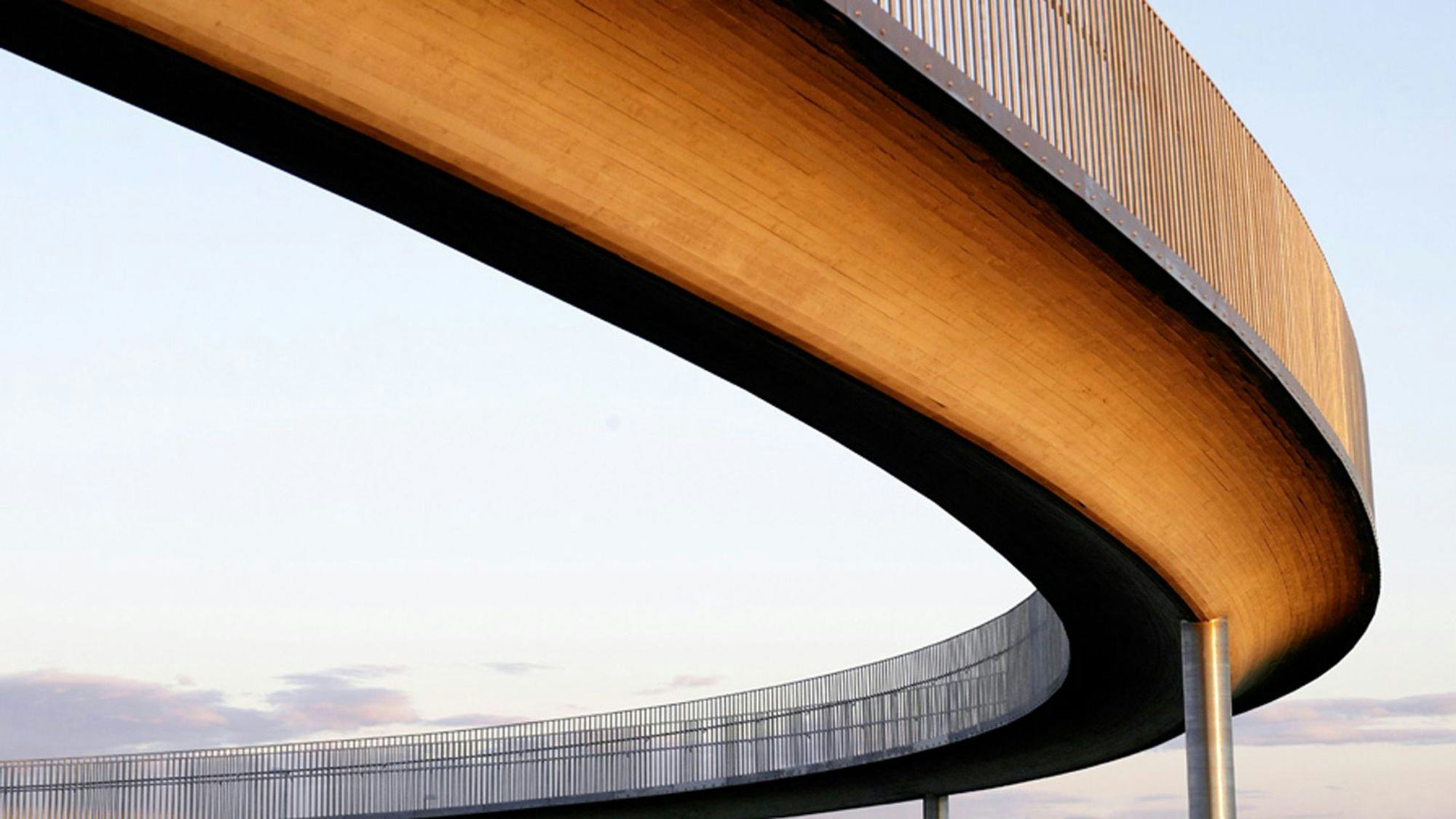 The photo shows a close-up of a curved bridge with a sleek design against a clear sky
