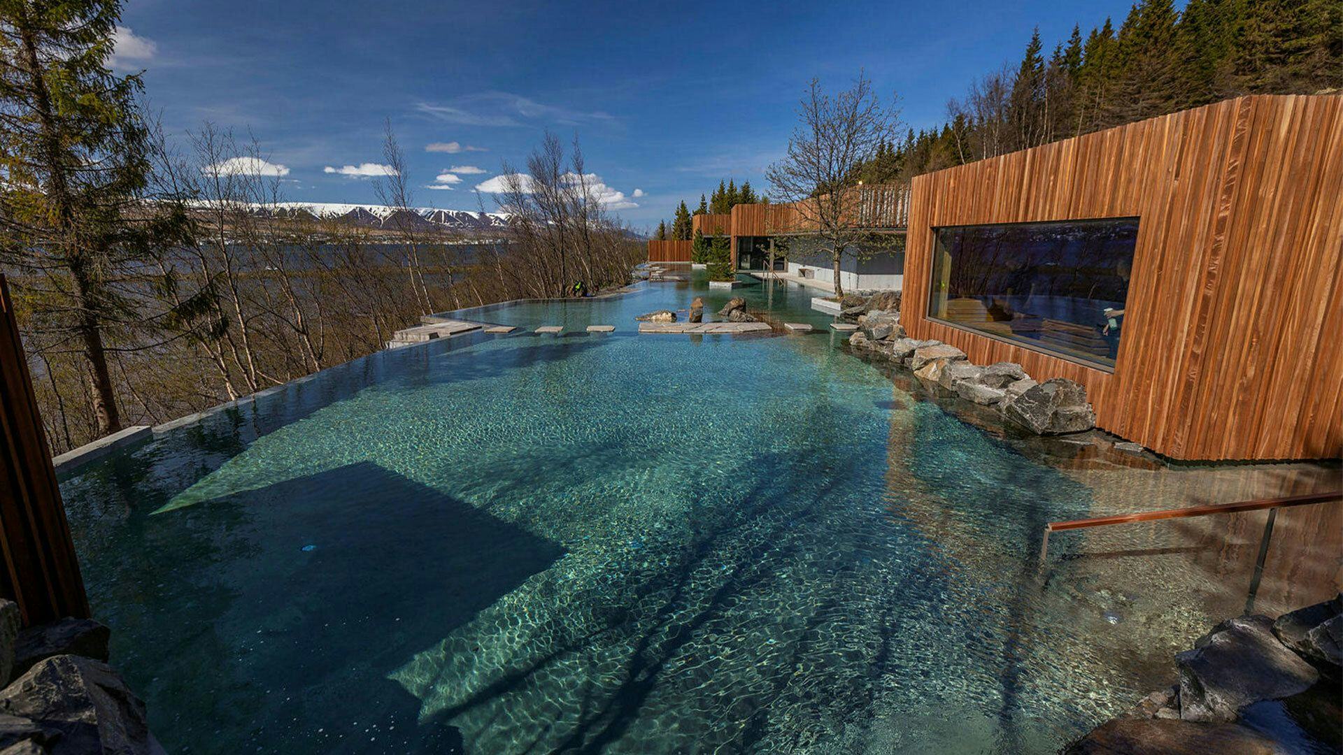 An outdoor thermal pool with clear blue water, surrounded by wooden structures and nature