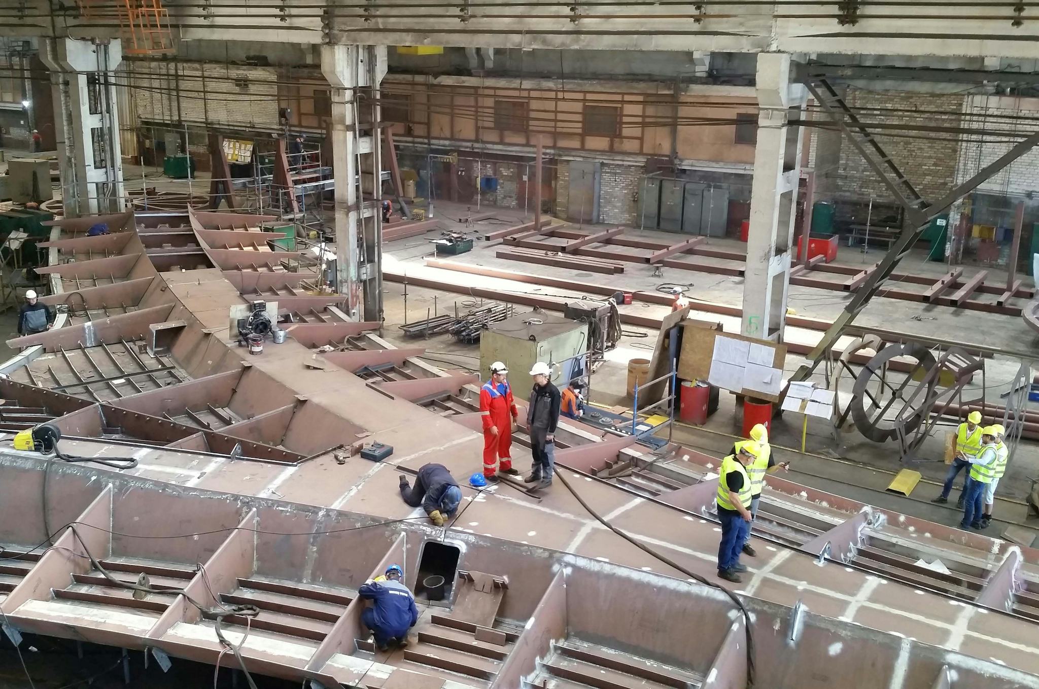 A group of workers in a large industrial facility, assembling steel structure