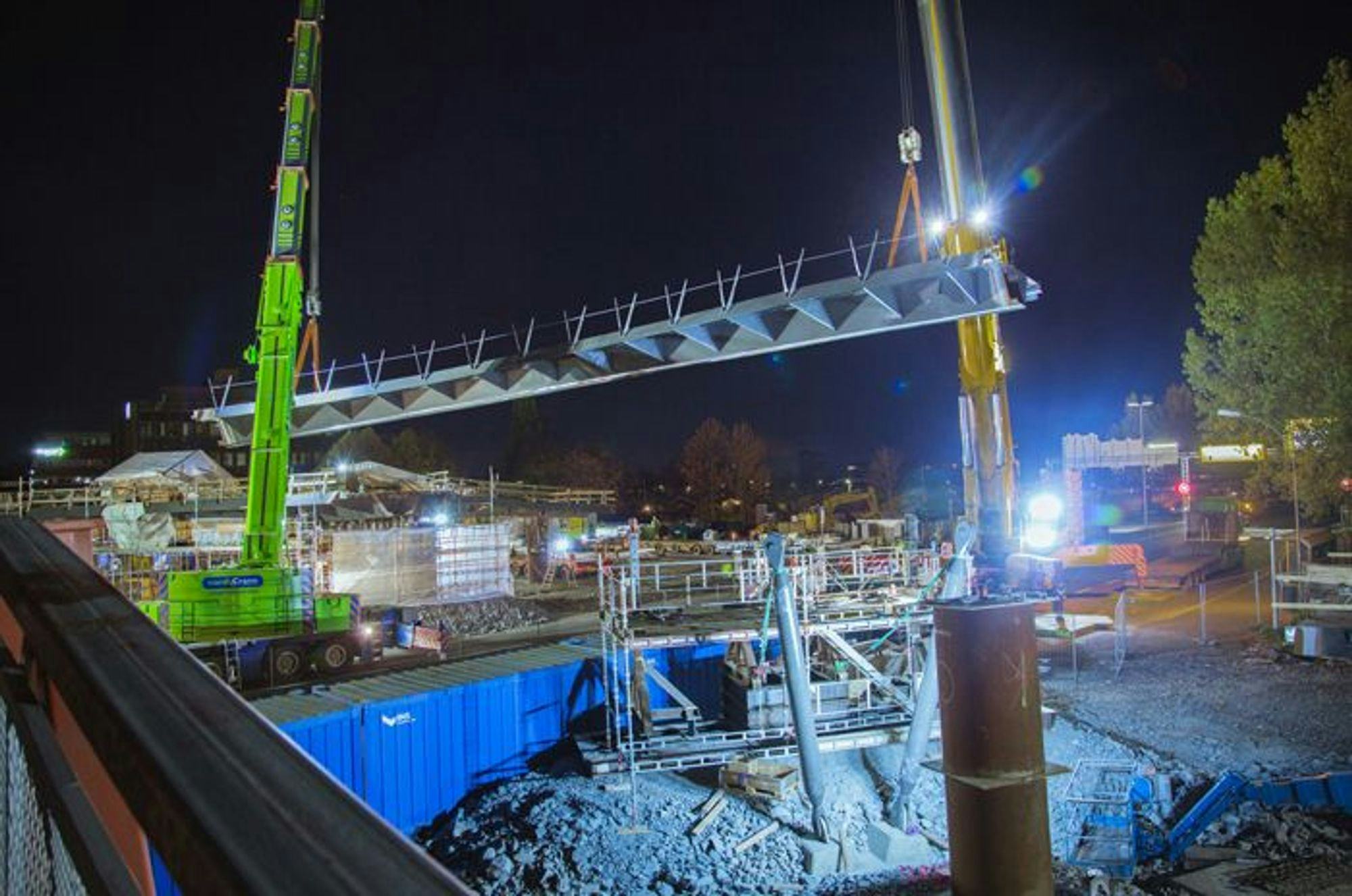 A construction site at night with a large crane lifting a section of a bridge