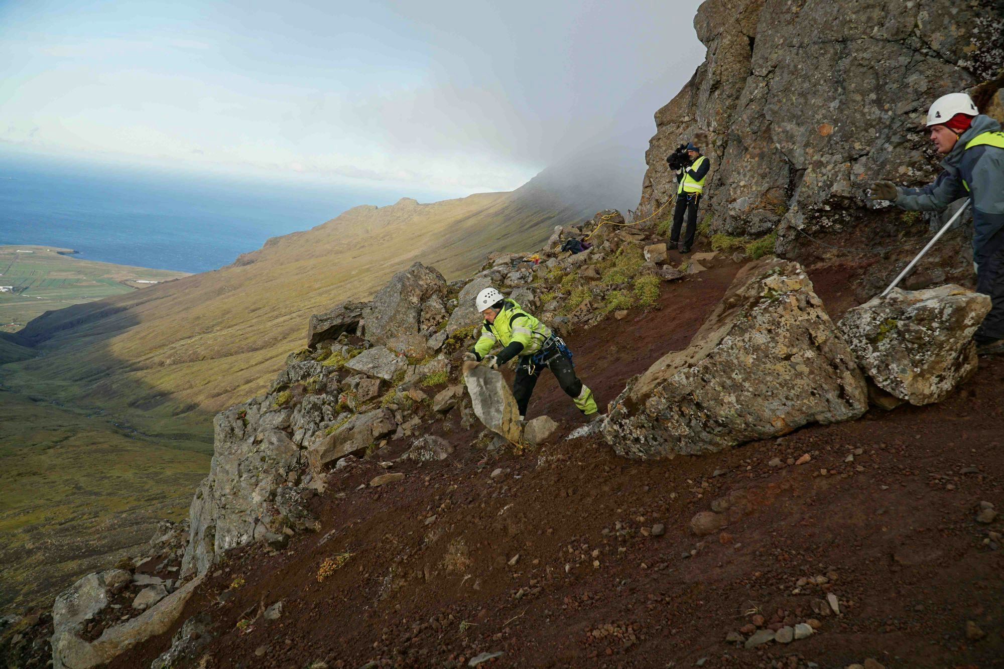 Three individuals wearing high visibility jacket, working on a rocky hillside 