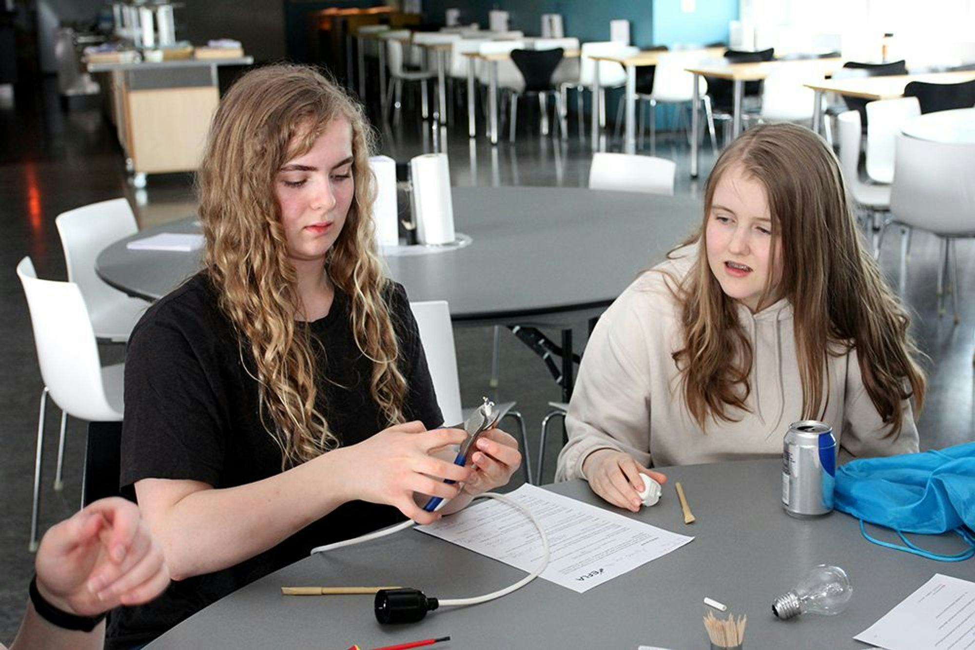 A girl cutting wires using plier next to another one observing the task with great focus