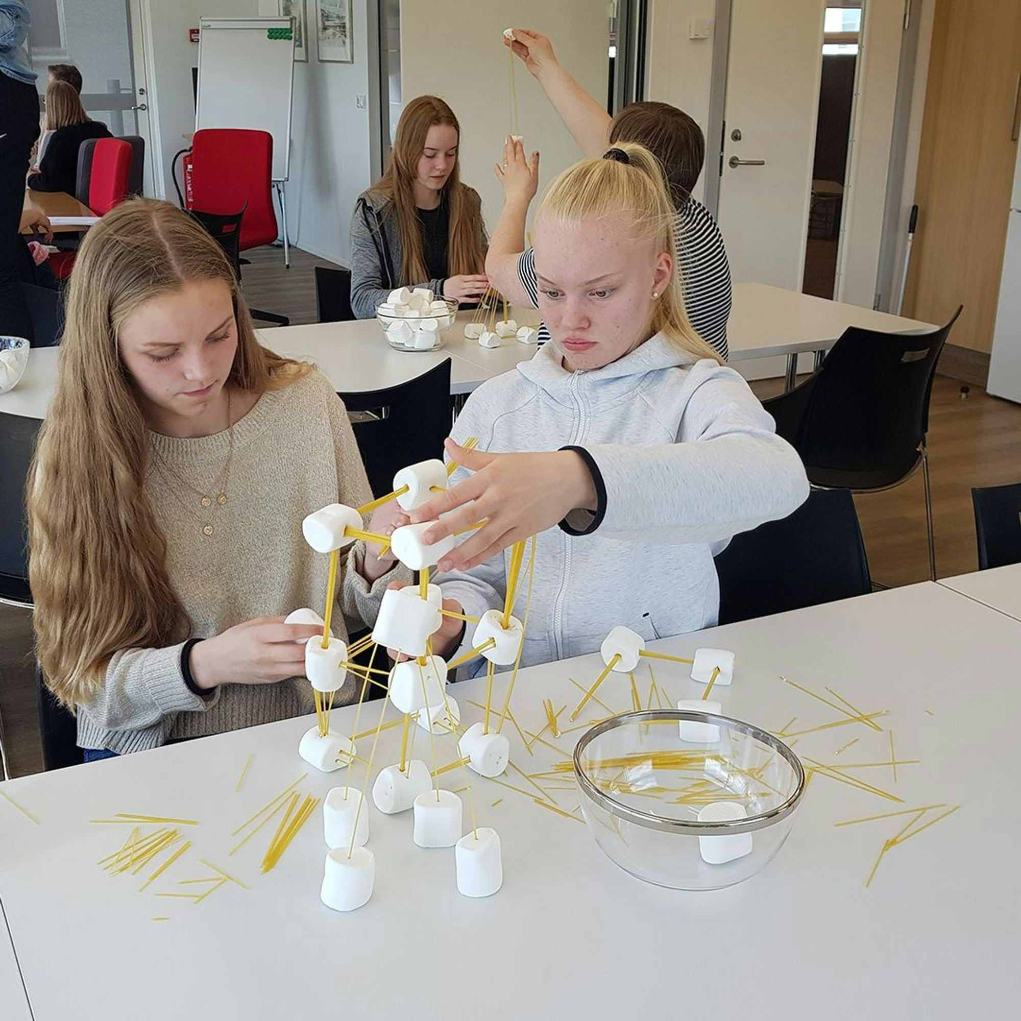 Two girls building something using spaghetti and marshmallow 
