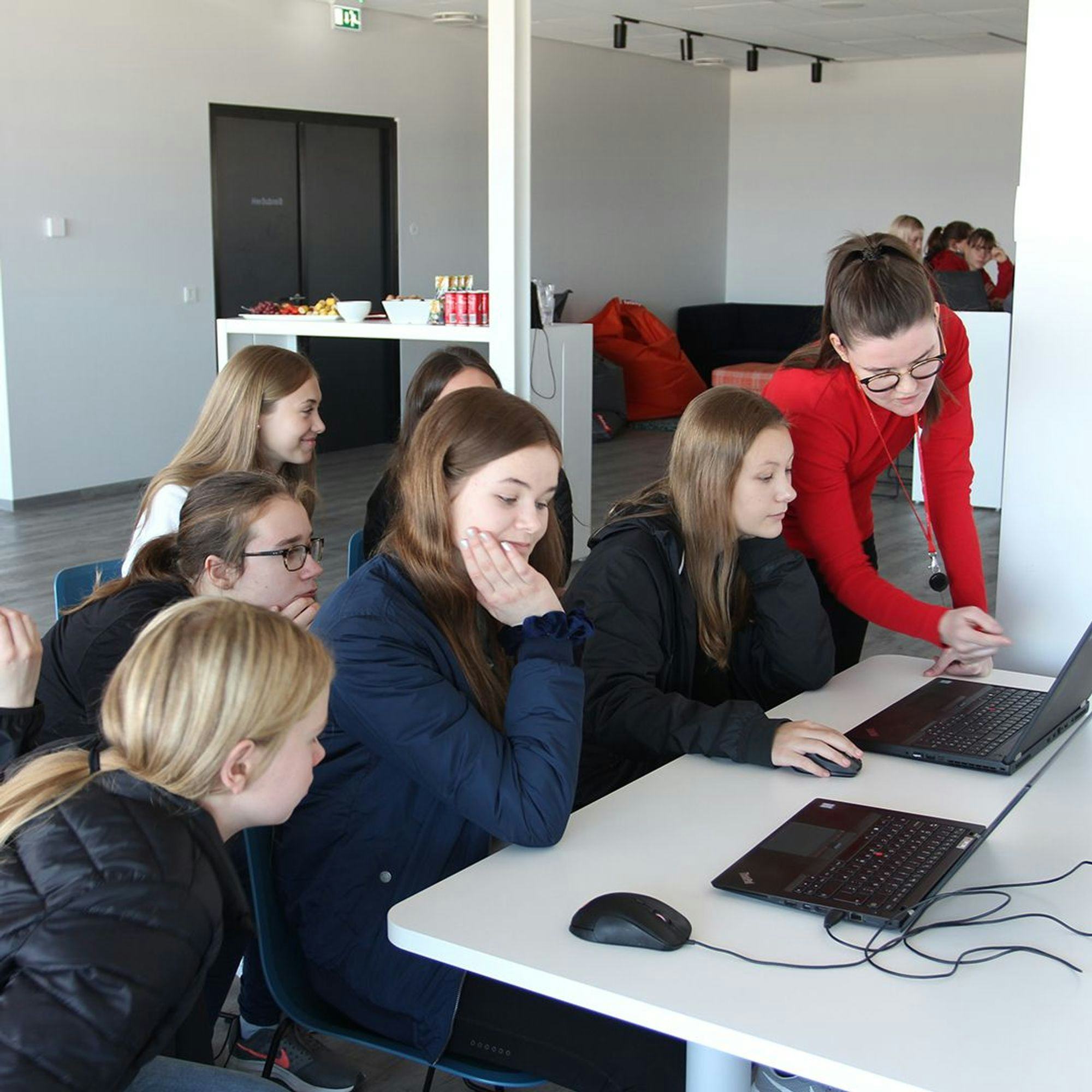 A woman giving instruction to six girls who are seated and looking at computer monitors