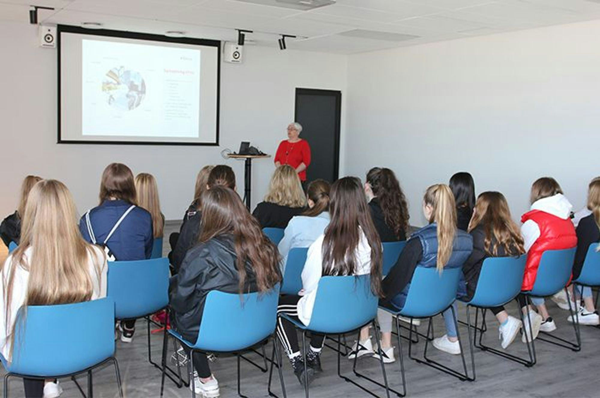 An audience of young girls facing a presenter next to a projection screen