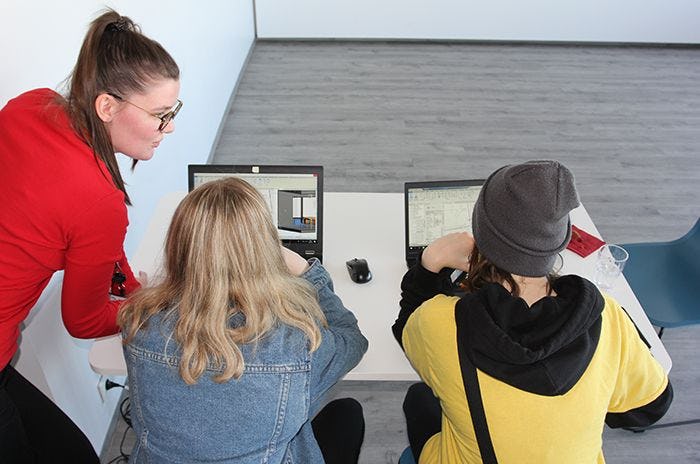 A woman giving instruction to two girls who are seated and looking at computer monitors