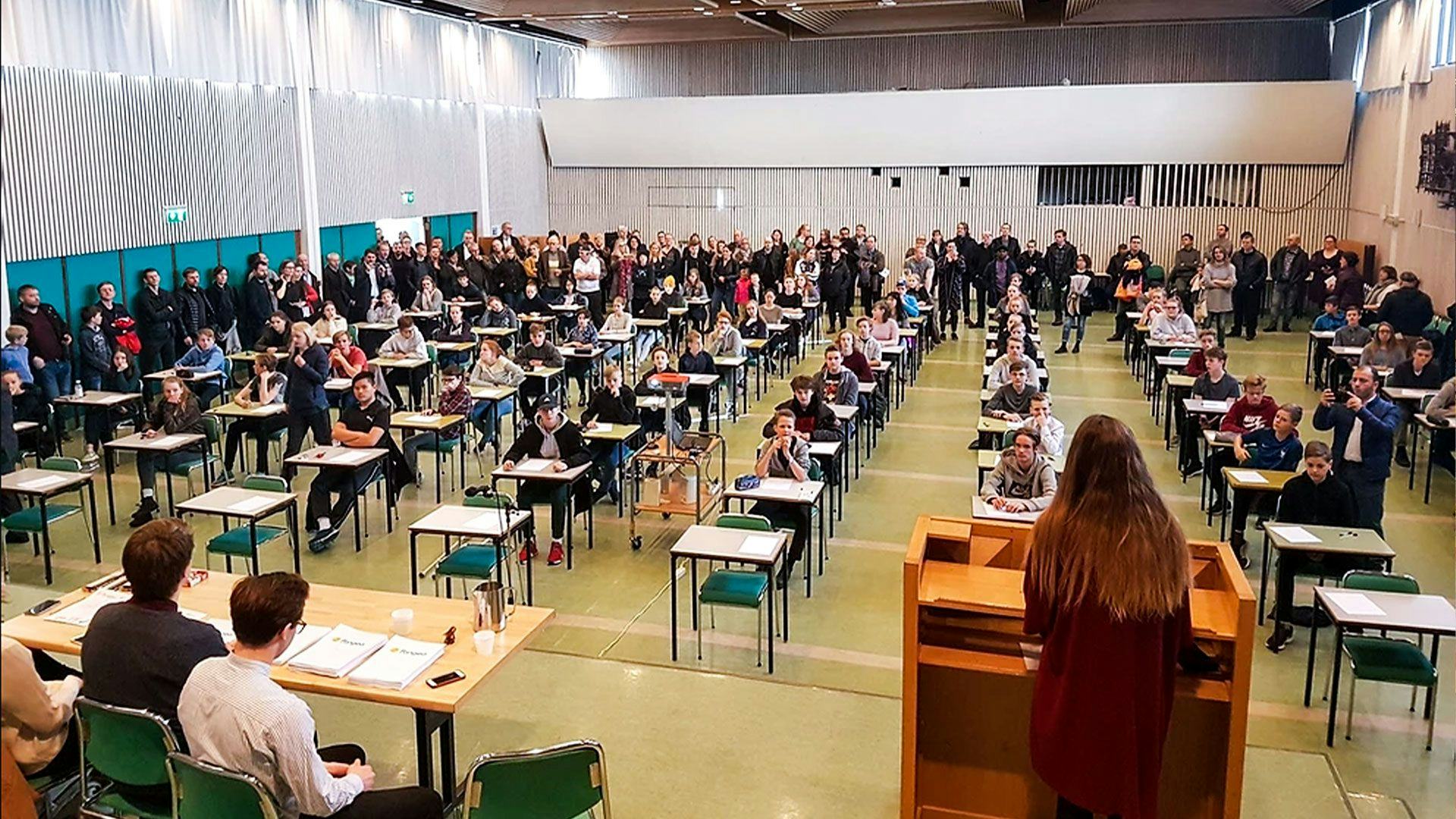 A large hall filled with rows of students seated at individual desks