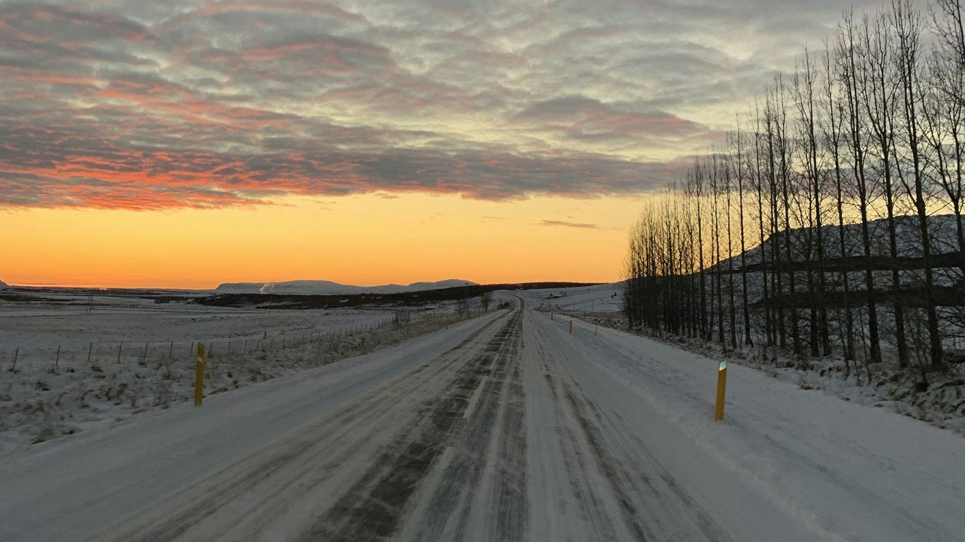A snow covered road leading into the distance under sunset sky 