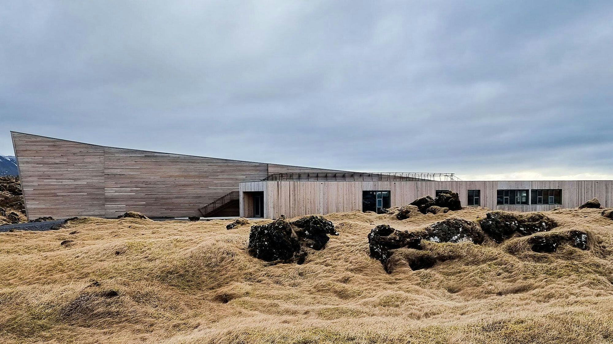 A modern building with unique curved wooden facade, set in rugged landscape with moss covered rocks