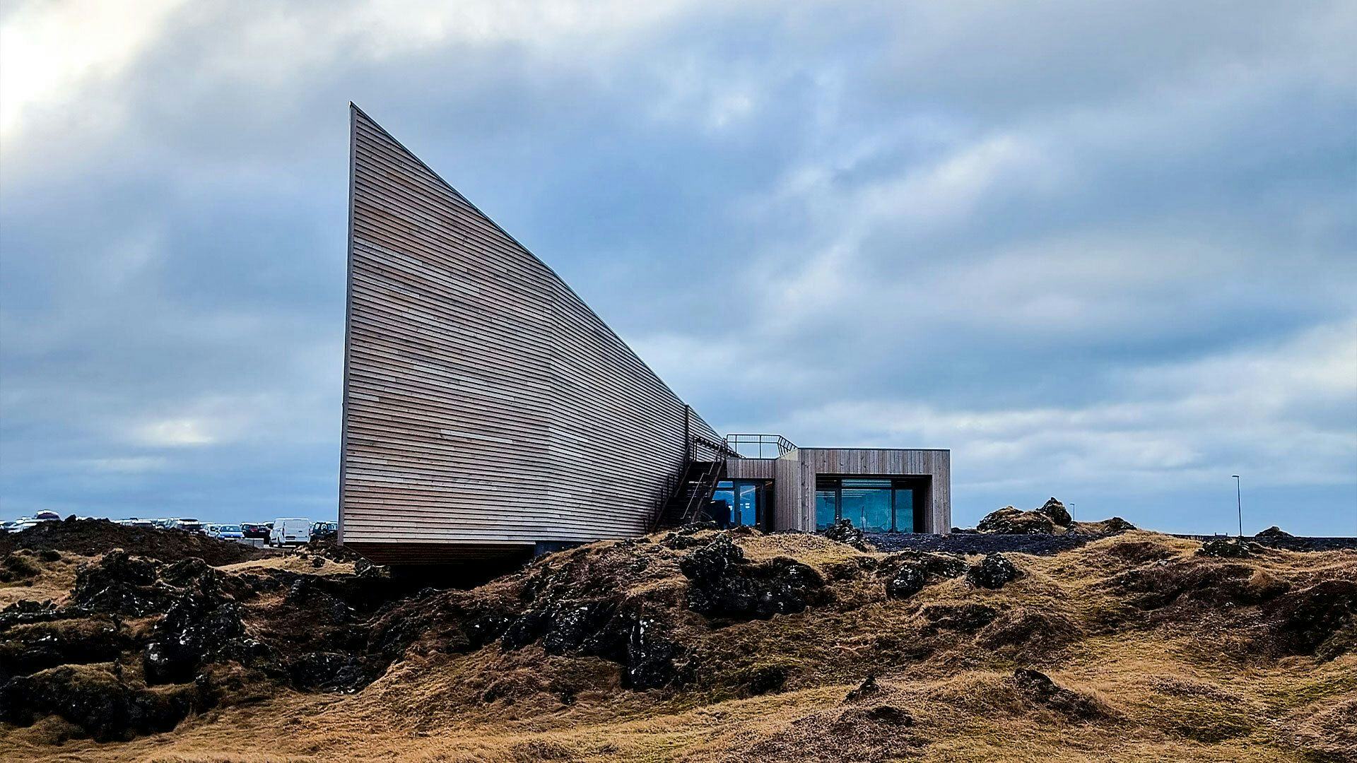 A modern building with unique angled facade, set in rugged landscape with moss covered rocks