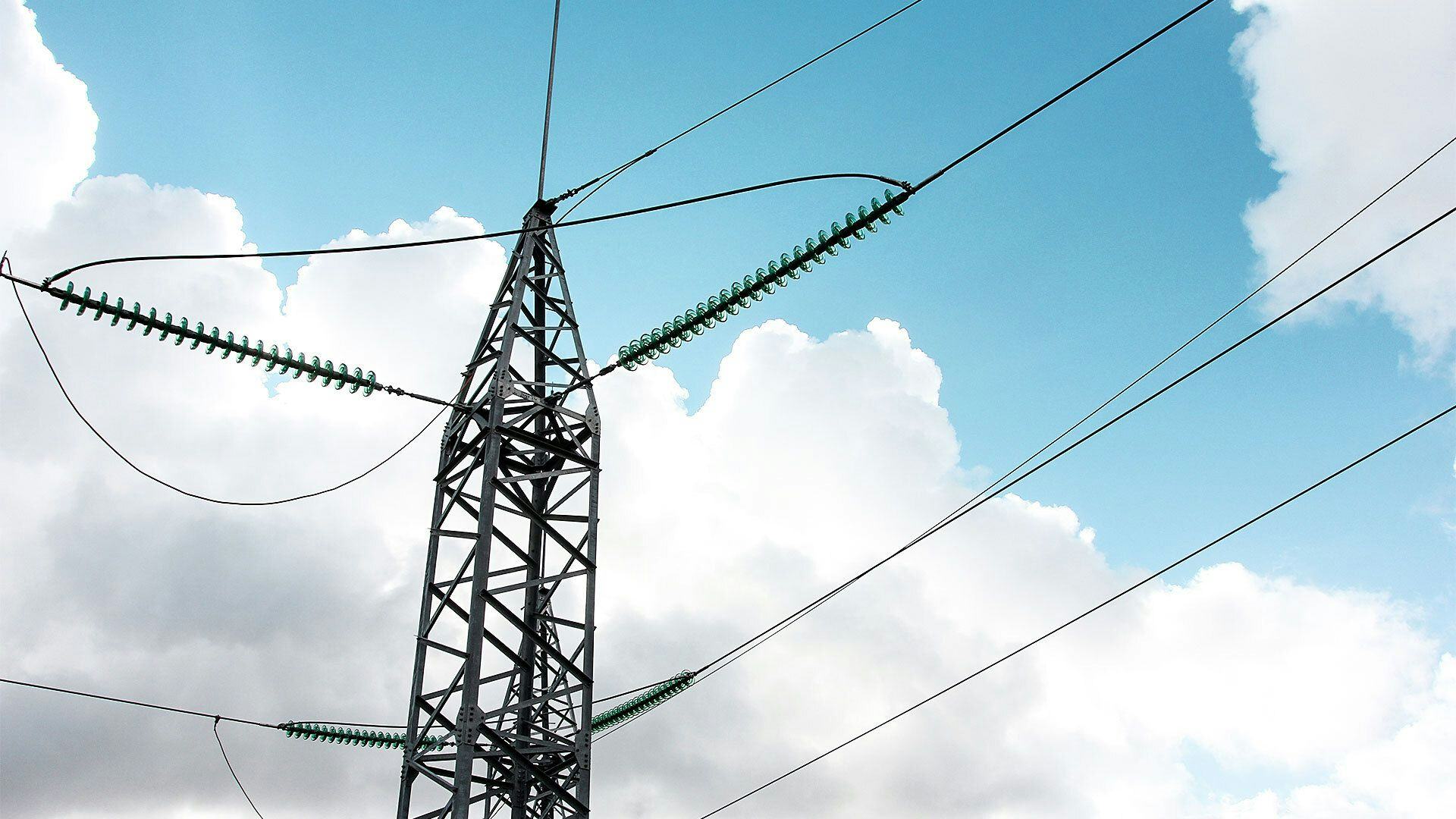 A close up photo of an electricity pylon with multiple cables against a backdrop of a cloudy blue sky