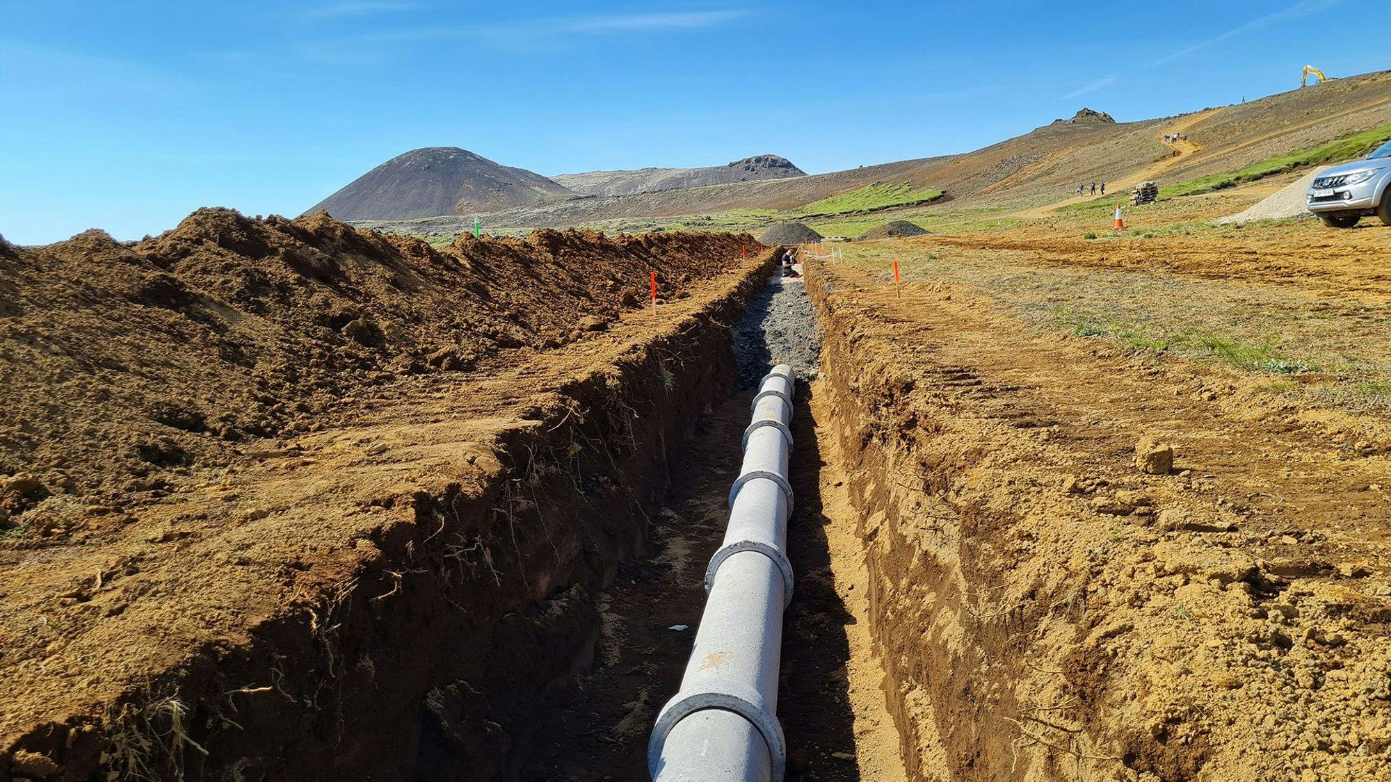 A long trench with a newly installed large white pipe