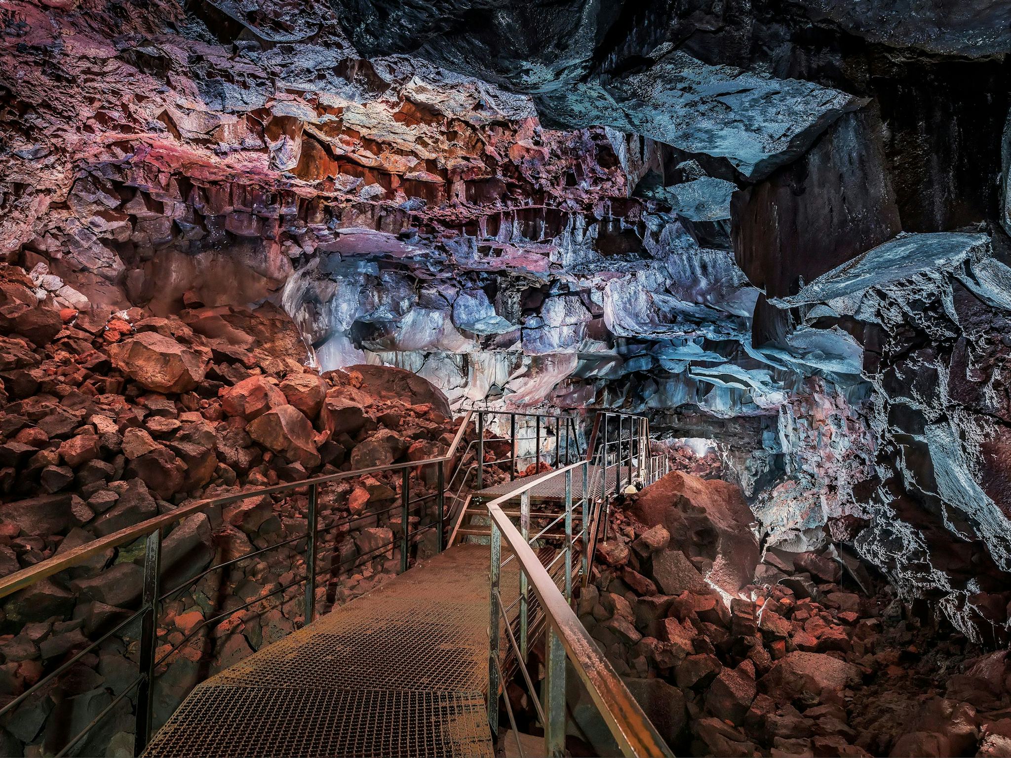 metal stairs leading towards red and blue stone wall in a cave
