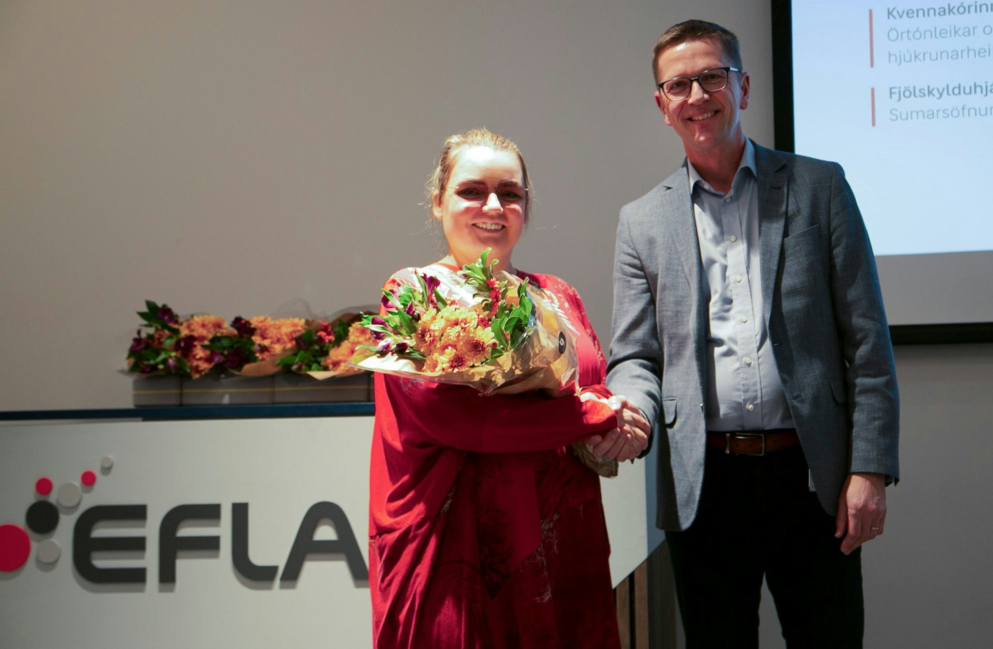 Two individuals shaking hands, one holding bouquet of flowers