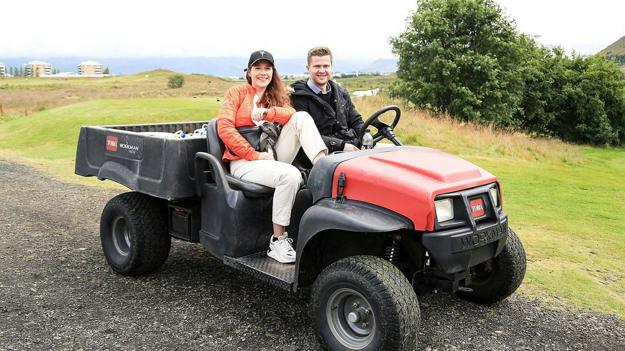 Two individuals seated on a red and black golf utility vehicle