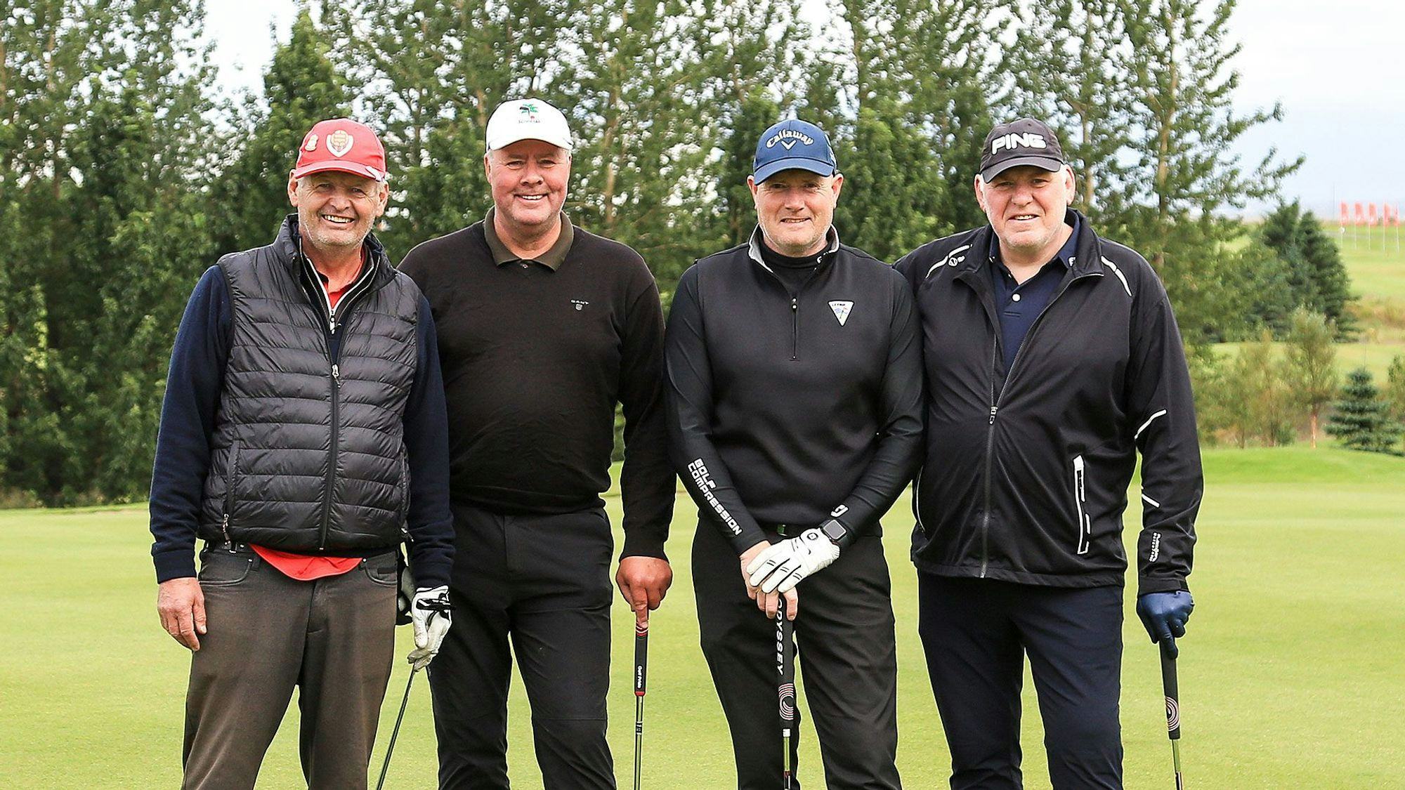 Four men wearing golf attire and caps, standing close together on a golf course