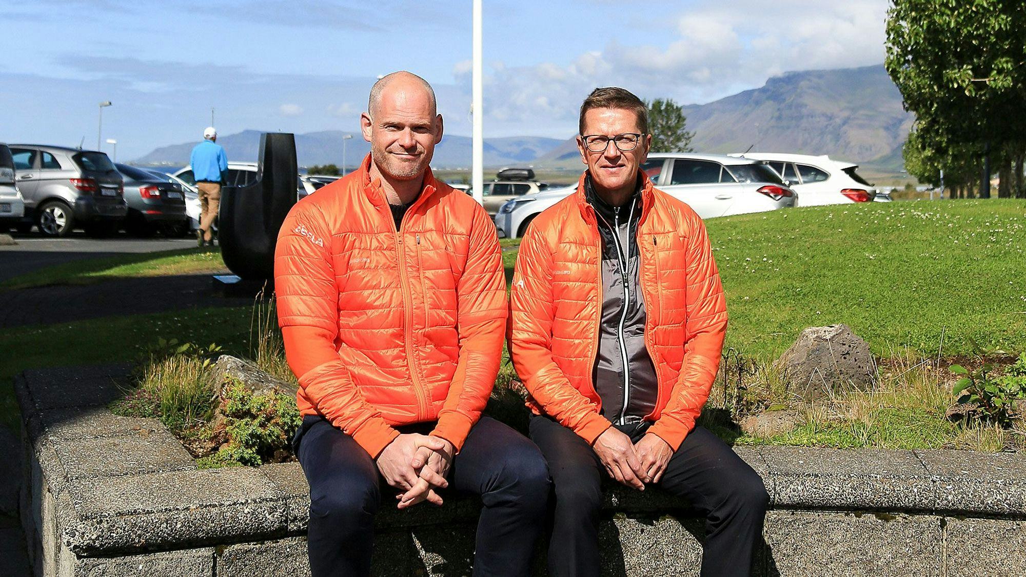Two men in matching bright orange jacket seated outdoor