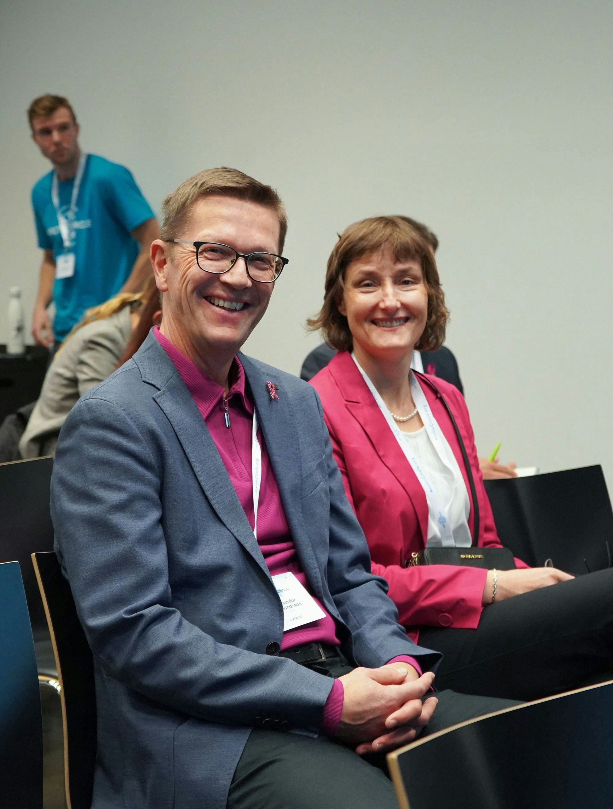 A man and a woman smiling and sitting together, both wearing pink with conference badges